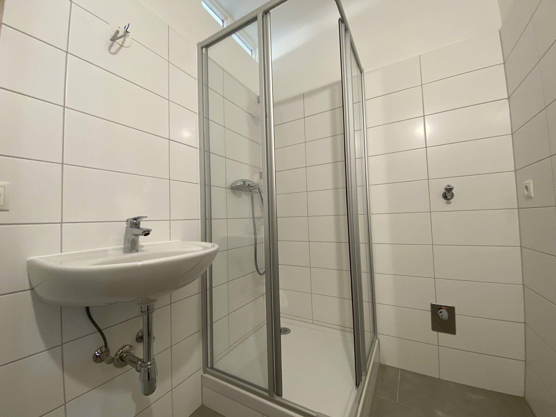 Modernes Badezimmer mit weißen Fliesen, Dusche und Waschbecken, in gutem und gepflegtem Zustand.