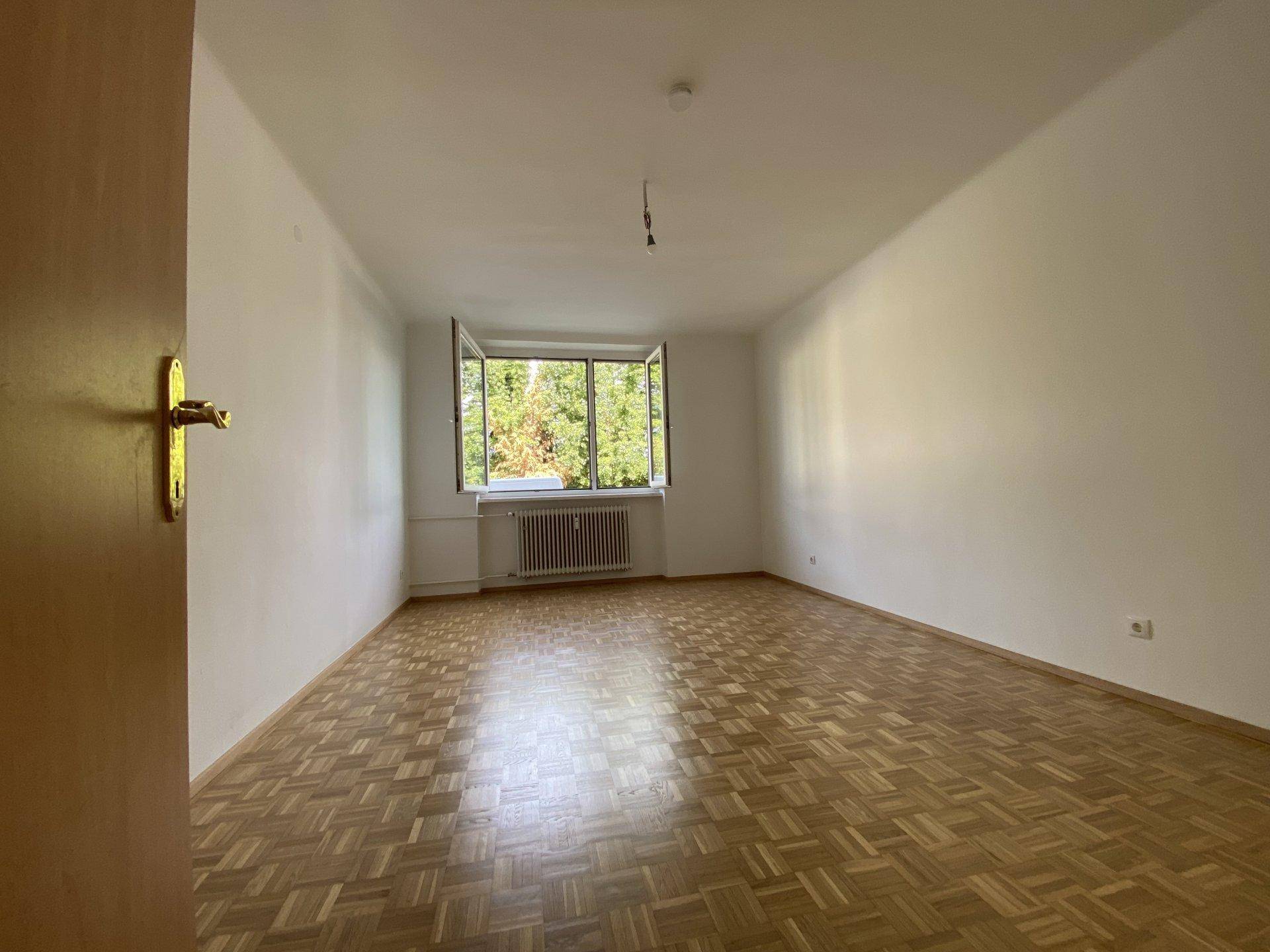 Geräumiges Zimmer mit Parkettboden und einem Fenster, das einen angenehmen Blick ins Grüne bietet.