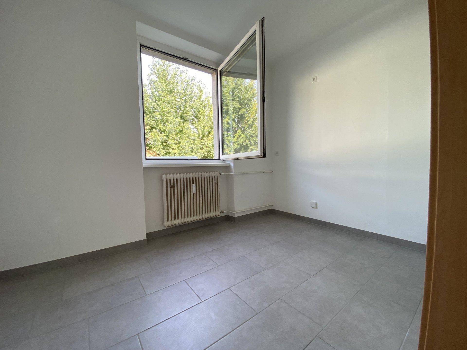 Leerer Raum mit großem Fenster, das viel Tageslicht hereinlässt und Blick ins Grüne bietet.