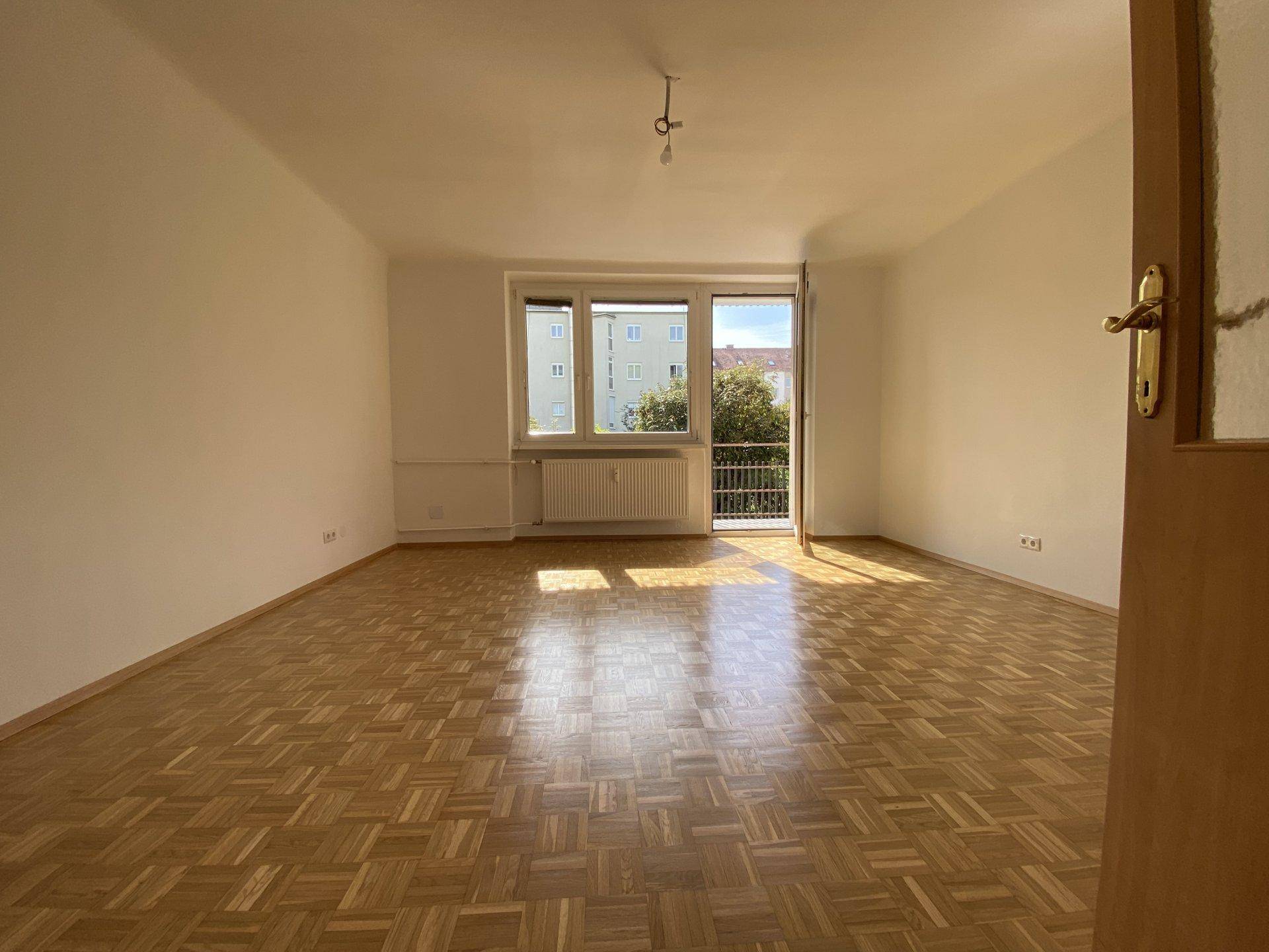 Geräumiges Wohnzimmer mit Parkettboden, viel Tageslicht und direktem Zugang zu einem Balkon.