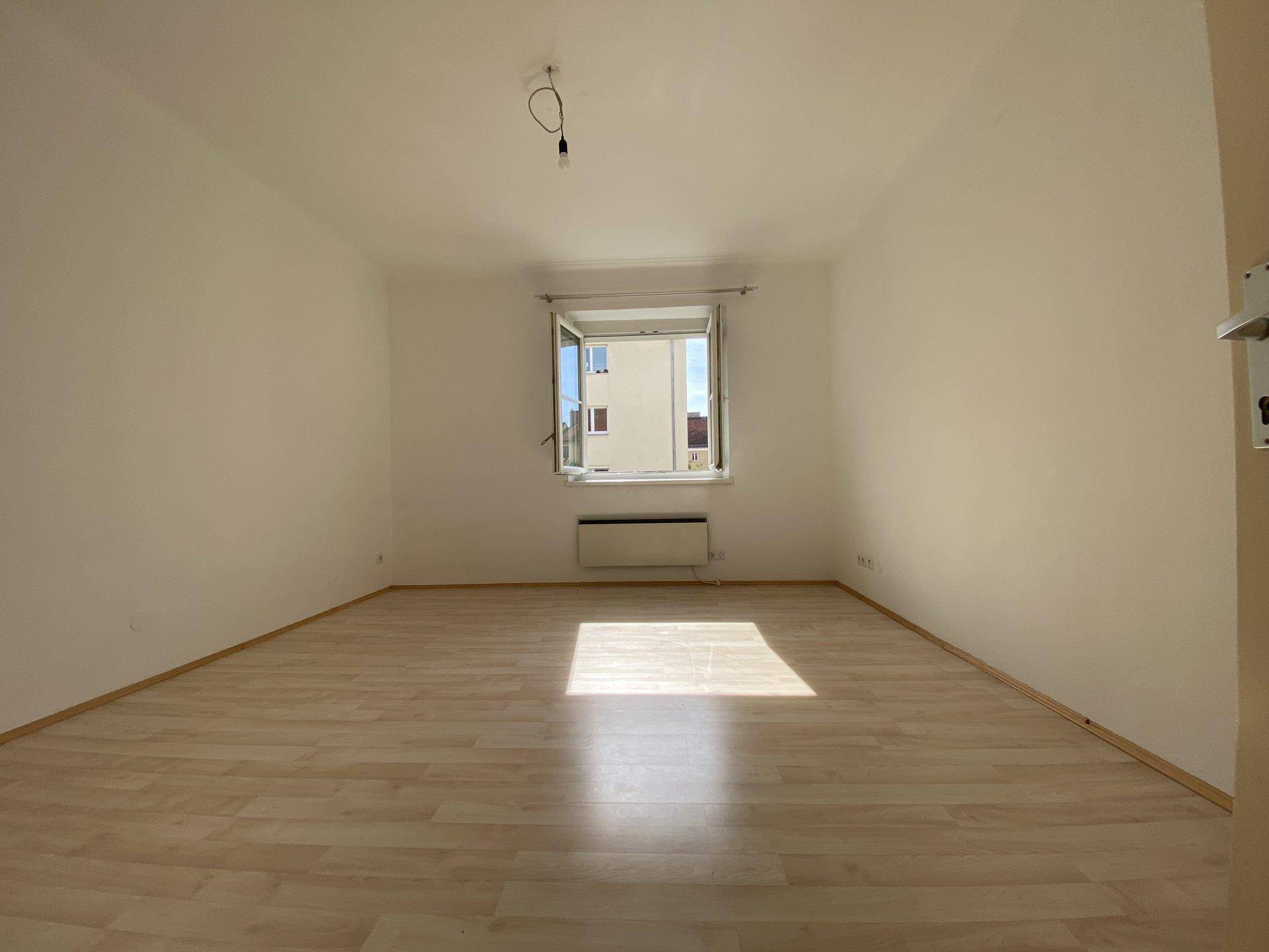 Geräumiges, leeres Zimmer mit Laminatboden und viel natürlichem Licht durch das Fenster.