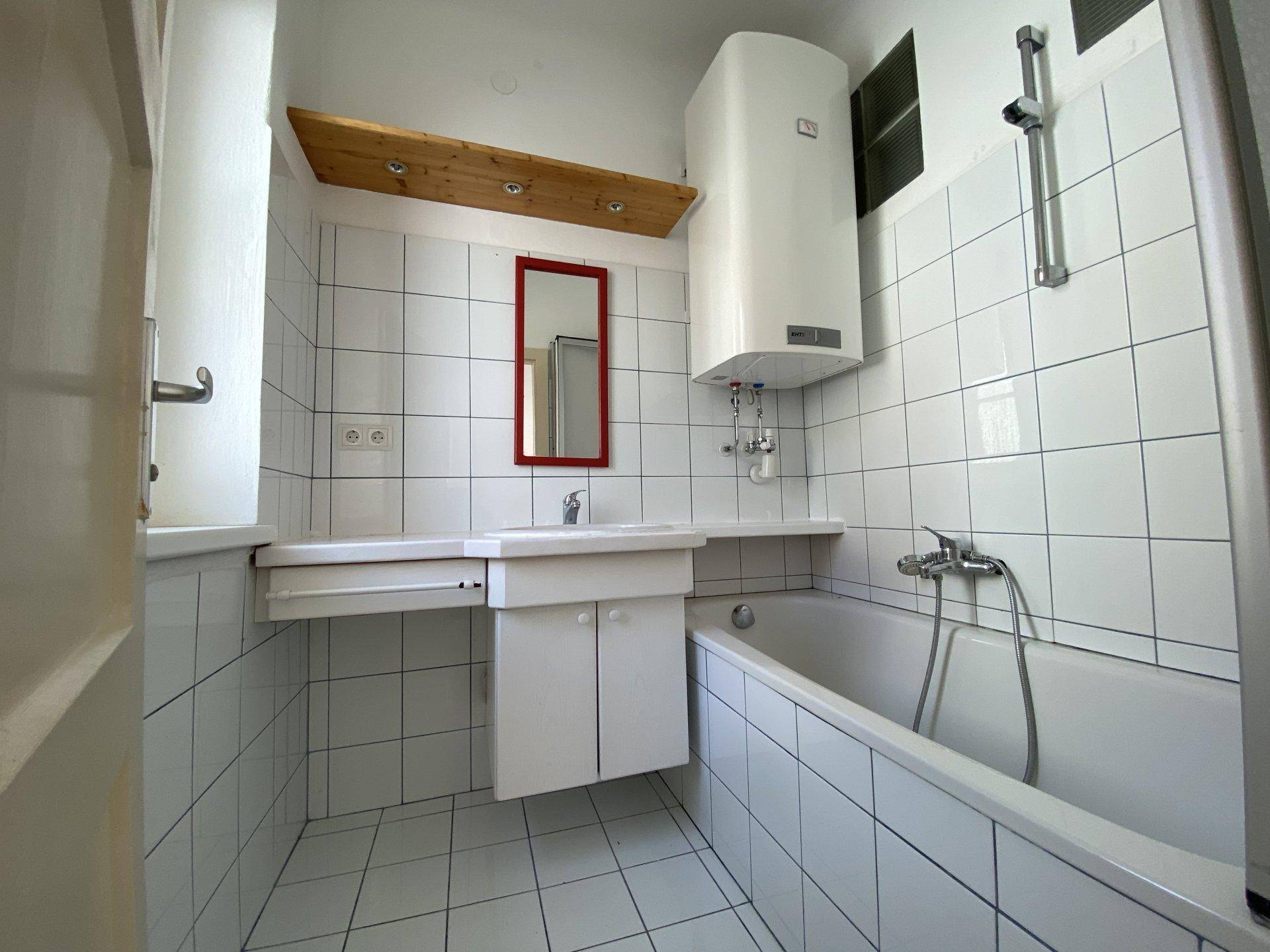 Gefliestes Badezimmer mit Badewanne, Duschfunktion, Waschbecken und Warmwasserboiler.
