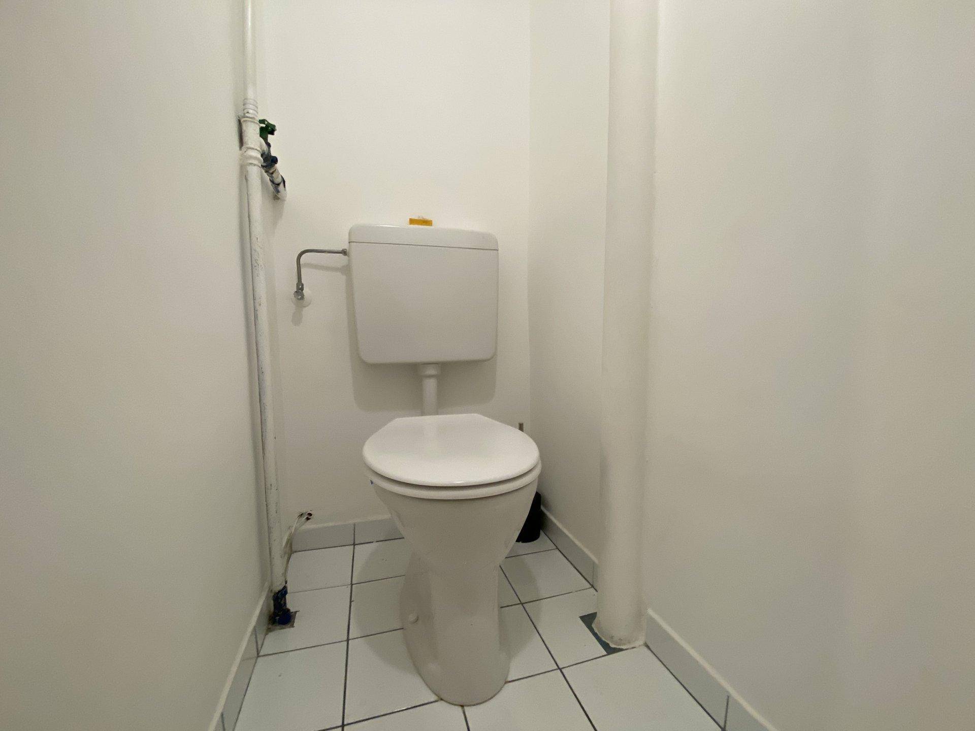Kleines separates WC mit weißer Toilette und hellen Fliesen an Boden und Wänden.