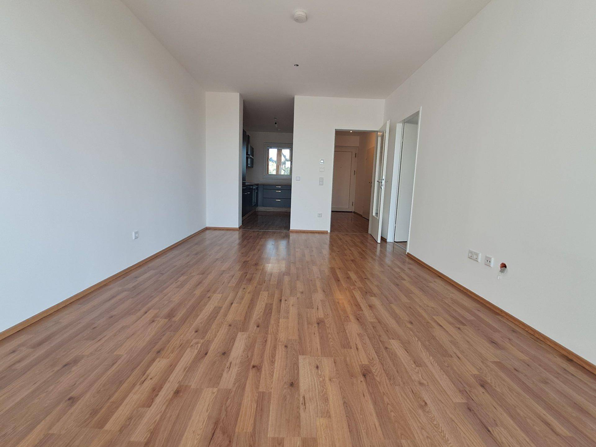 Heller Wohnbereich mit Laminatboden und offenem Übergang zur Küche.