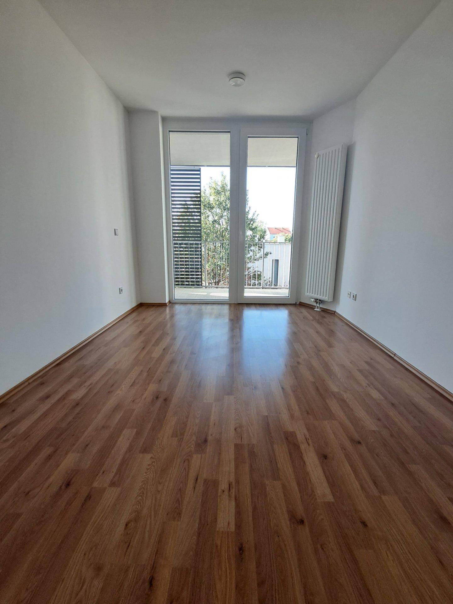Heller Raum mit Laminatboden, großen Fenstern und Zugang zum Balkon.