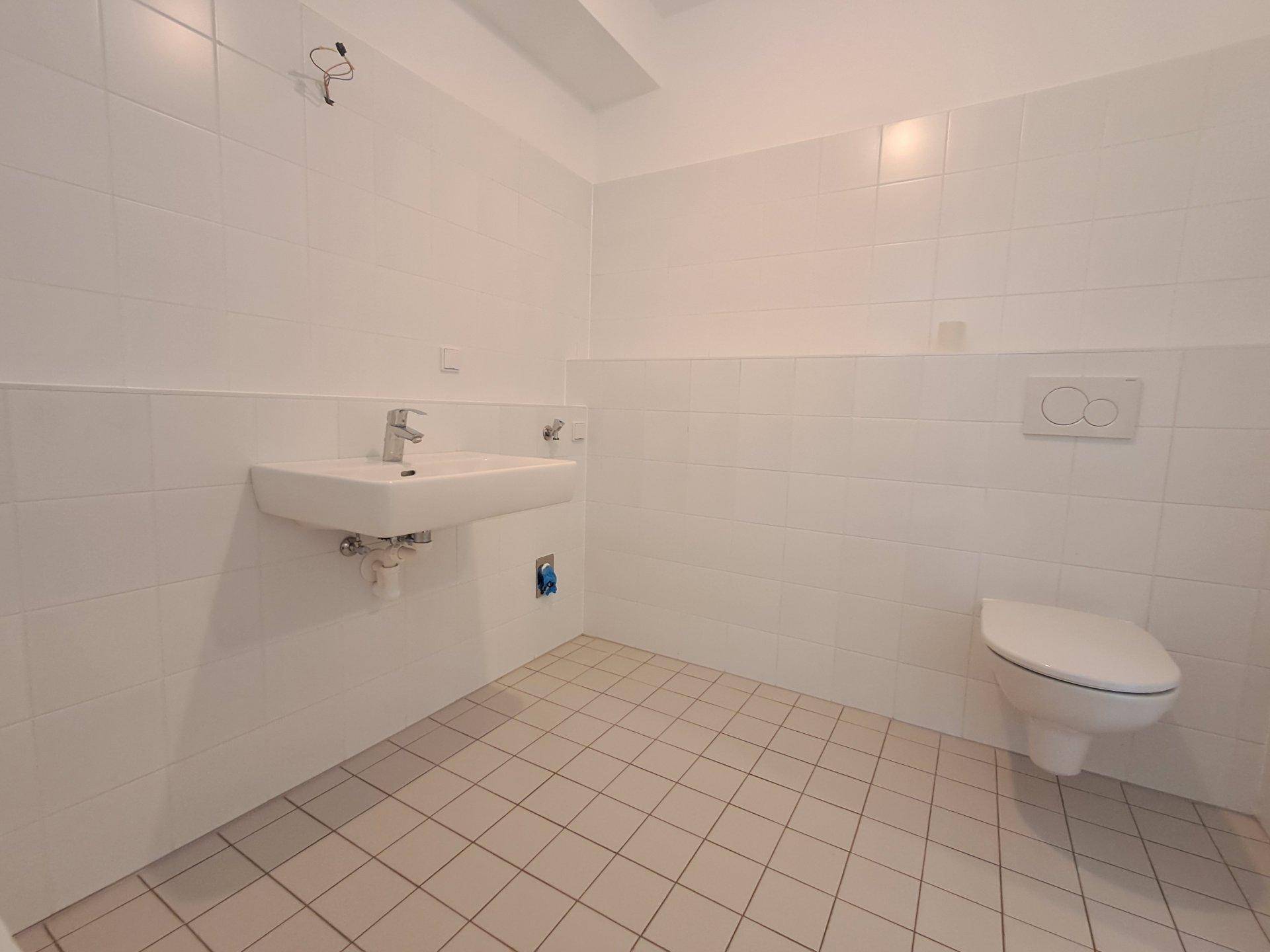 Helles Badezimmer mit wandhängendem WC, Waschbecken und weißen Fliesen.