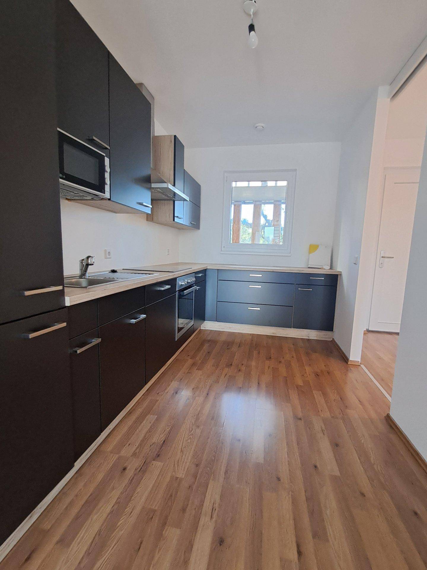 Geräumige Küche mit dunklen Schränken, Laminatboden und Fenster mit Blick ins Grüne.