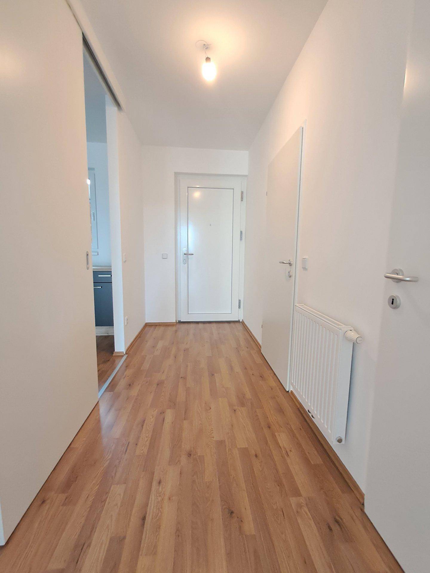 Heller Flur mit Laminatboden, weißen Wänden und Zugang zu weiteren Räumen.