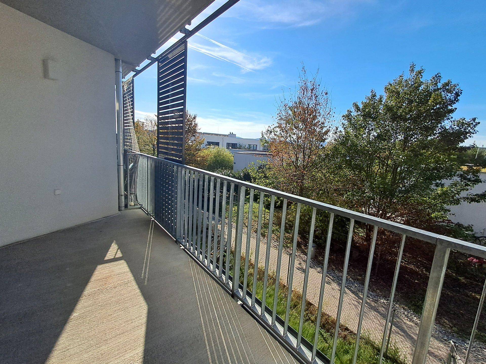 Geräumiger Balkon mit Metallgeländer und Blick ins Grüne an einem sonnigen Tag.
