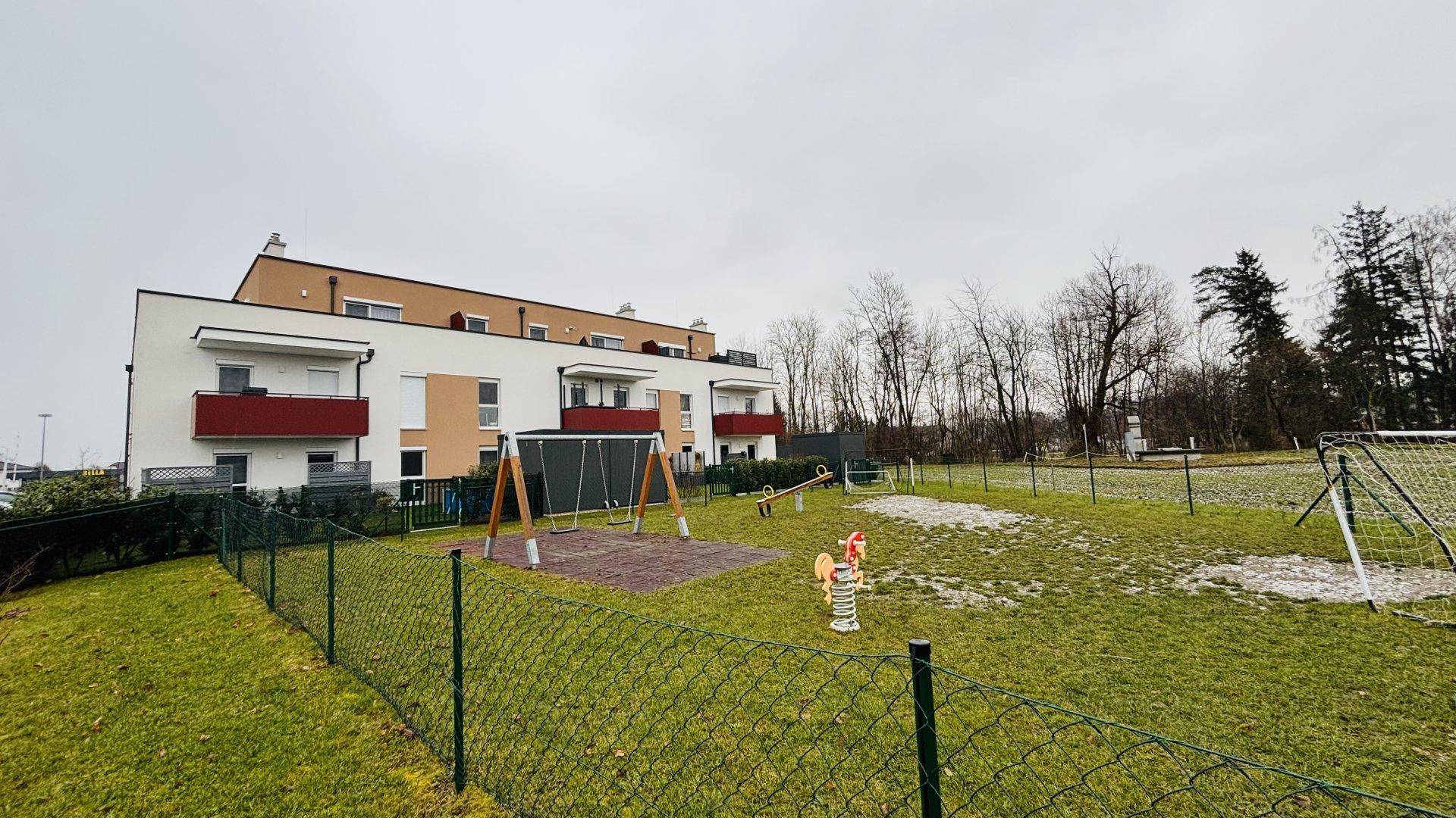 Modernes Wohngebäude mit angrenzendem Kinderspielplatz und weitläufigen Grünflächen.