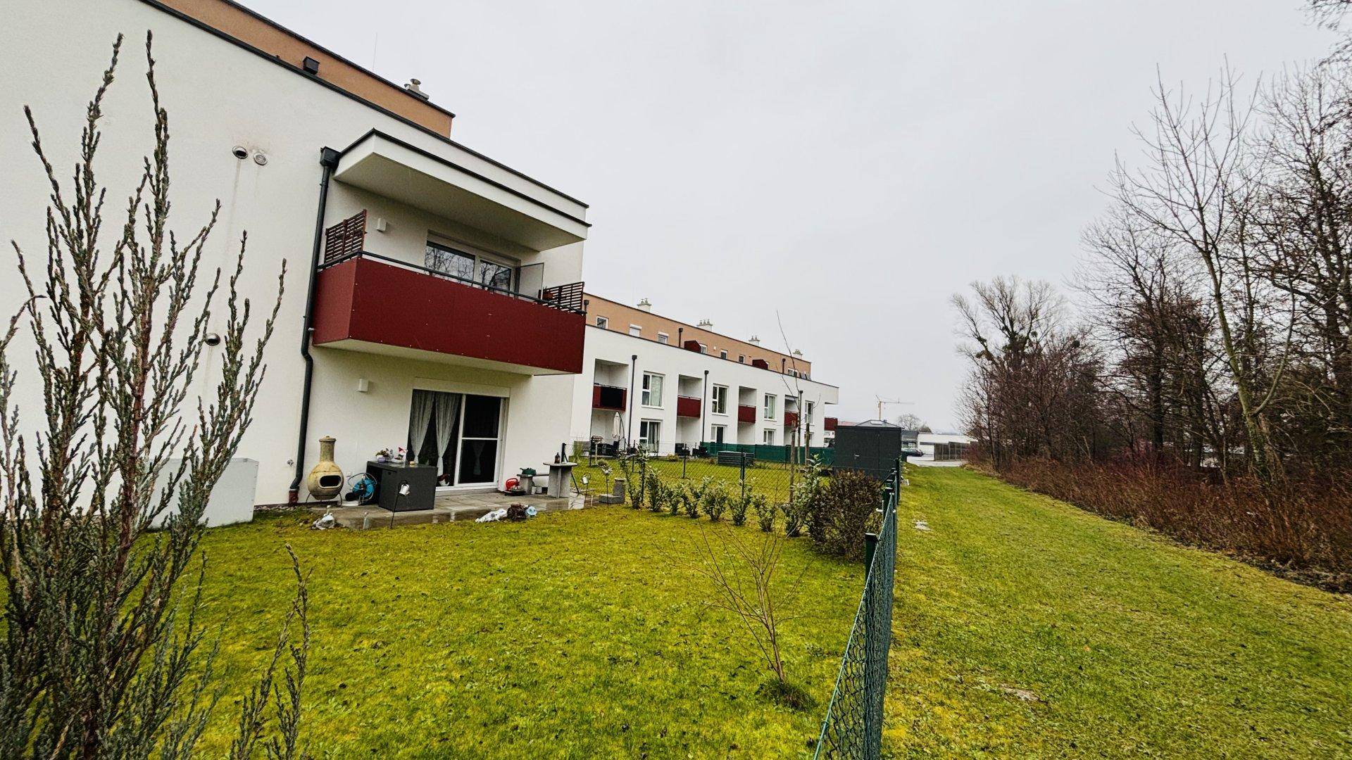 Seitenansicht des Wohngebäudes mit Rasenflächen, Terrassen und Balkonen in grüner Umgebung.