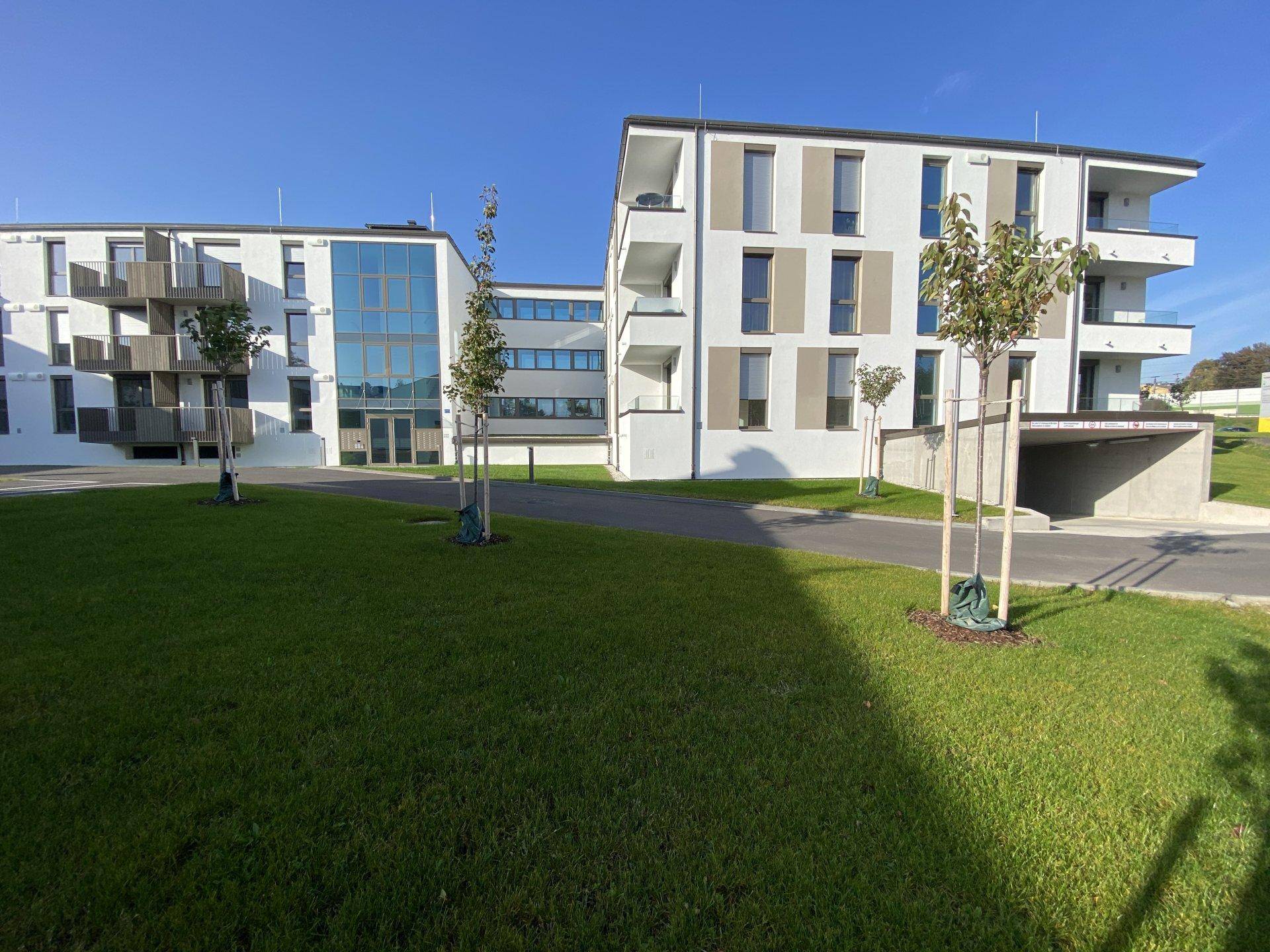 Mehrere moderne Wohngebäude mit Balkonen und Tiefgaragenzufahrt, umgeben von Grünflächen.