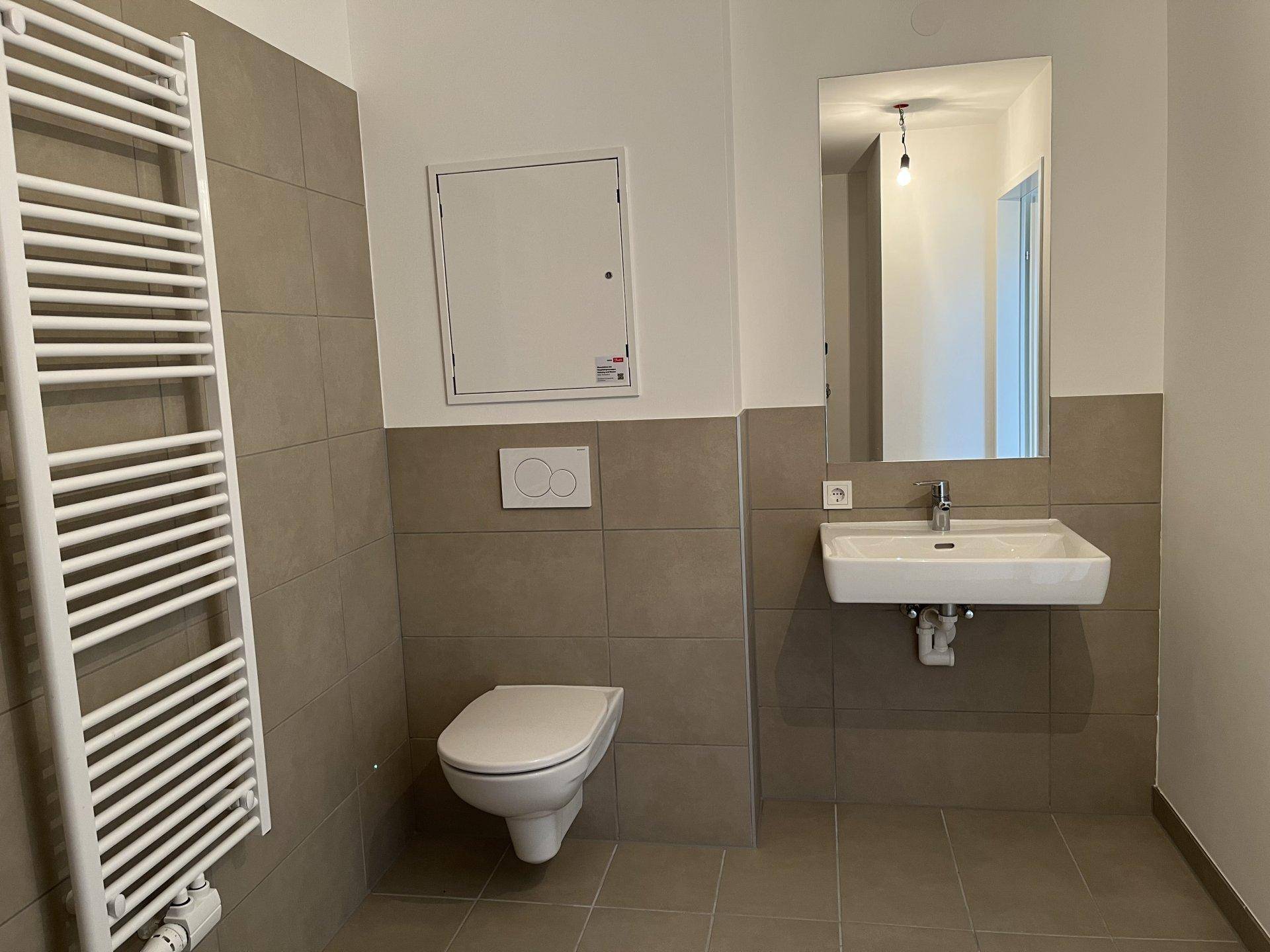 Modernes Badezimmer mit beigefarbenen Fliesen, wandhängendem WC und Handtuchheizkörper.