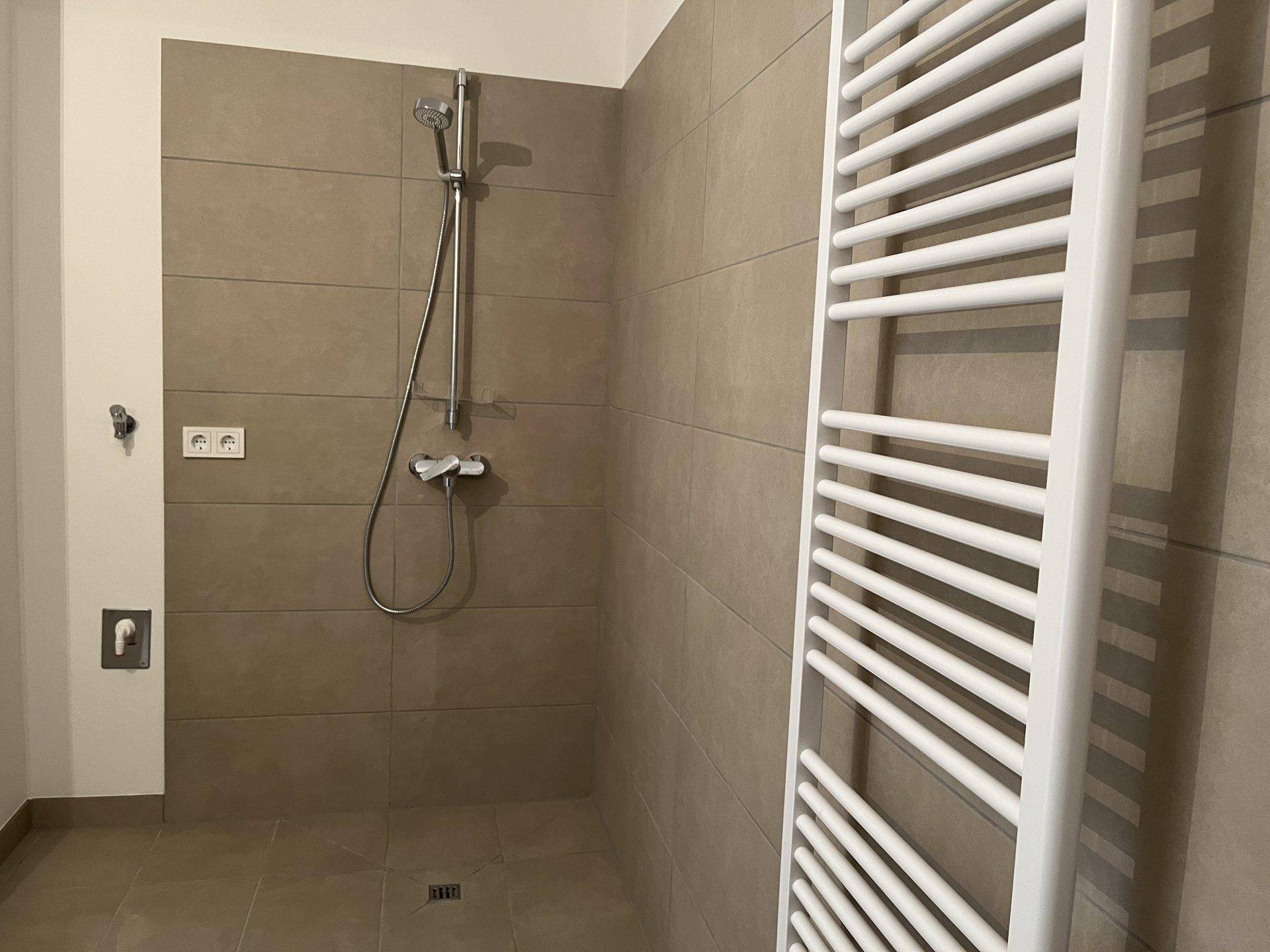 Duschbereich im modernen Badezimmer mit beigefarbenen Fliesen und Handtuchheizkörper.