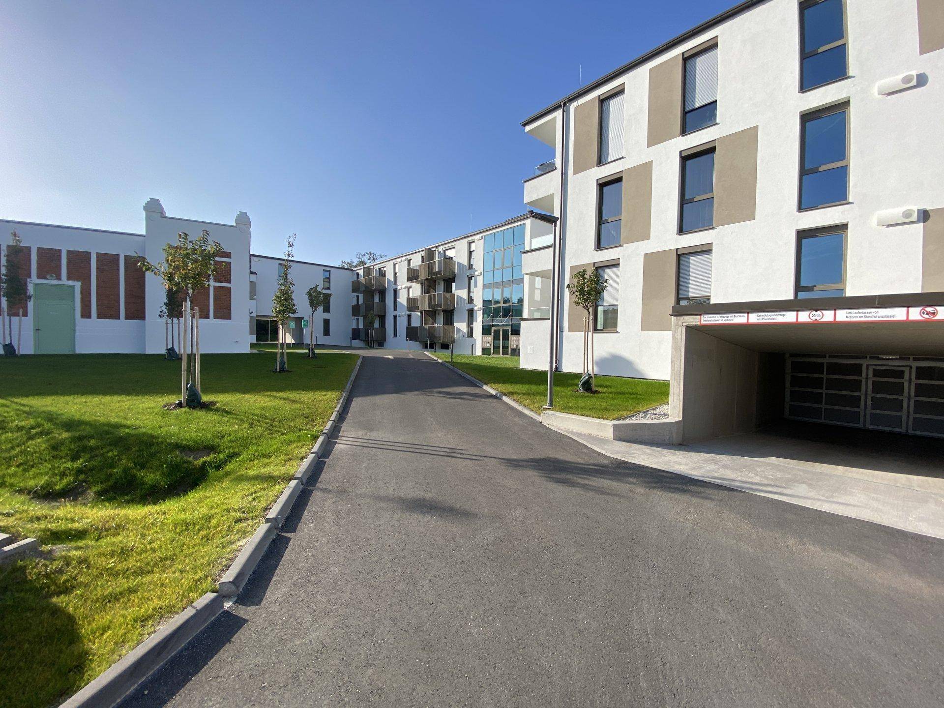 Zufahrt zur Tiefgarage eines modernen Wohnkomplexes mit angrenzenden Grünflächen.