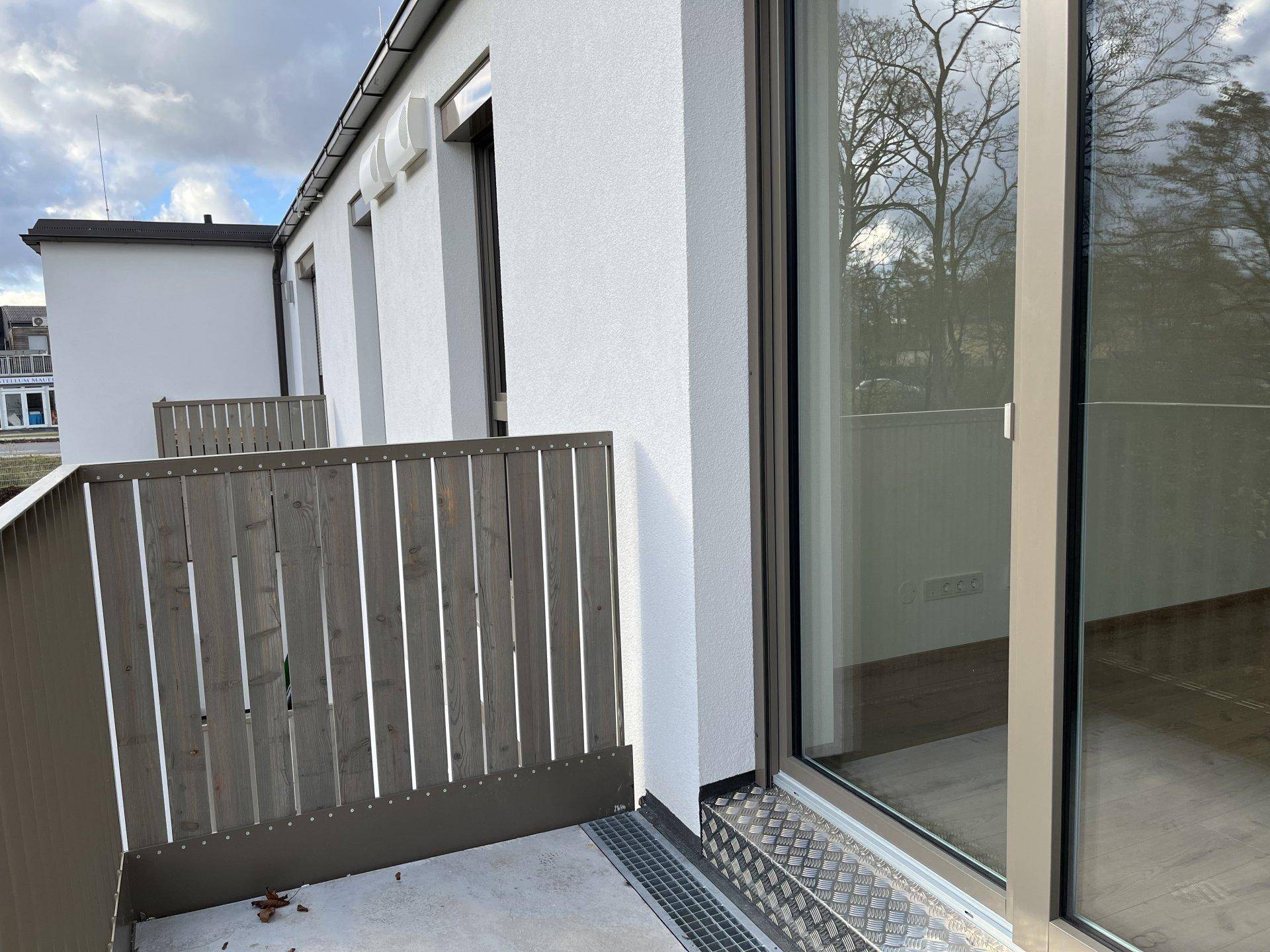 Kleiner Balkon mit Holzzaun und Blick auf die Umgebung, zugänglich durch eine Glastür.