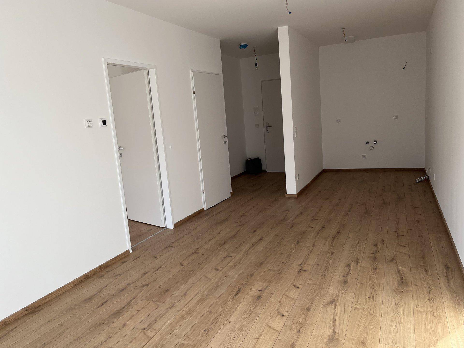 Heller Raum mit Laminatboden und Anschlüssen für eine zukünftige Küche.