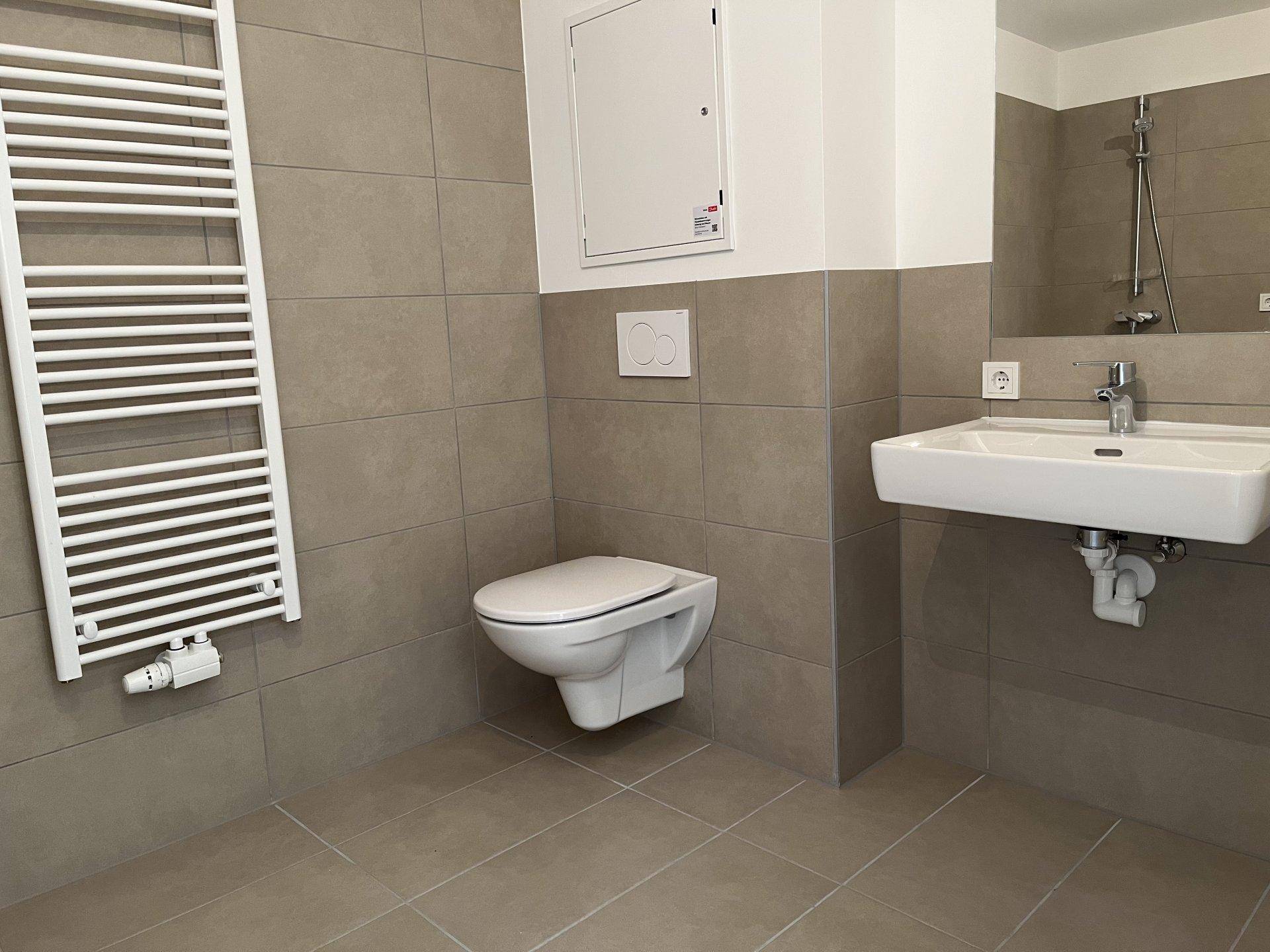 Modernes Badezimmer mit beigefarbenen Fliesen, wandhängendem WC und Waschbecken.