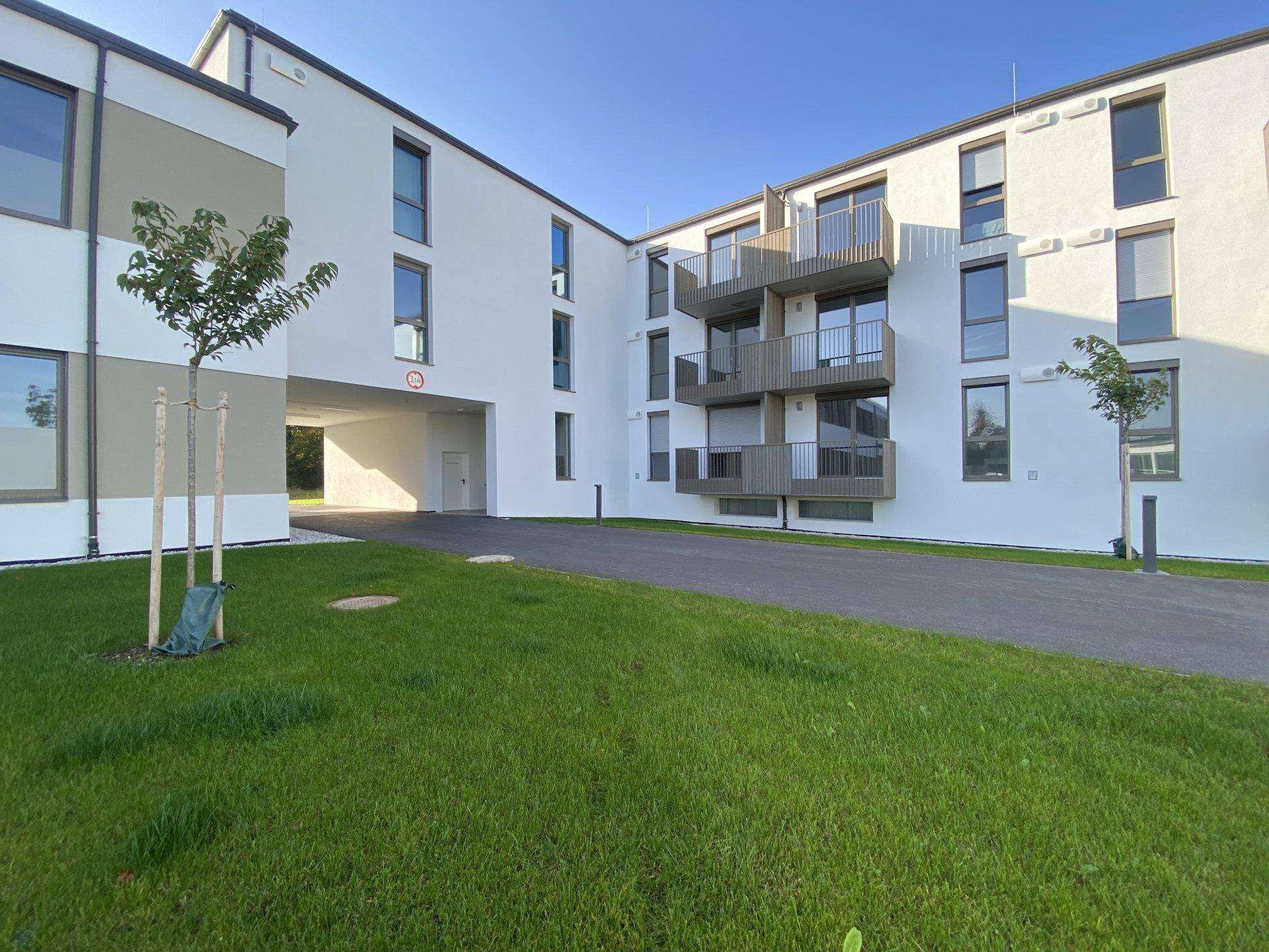 Moderne Wohnanlage mit weißer Fassade, Balkonen und Zufahrt zu einem überdachten Bereich.