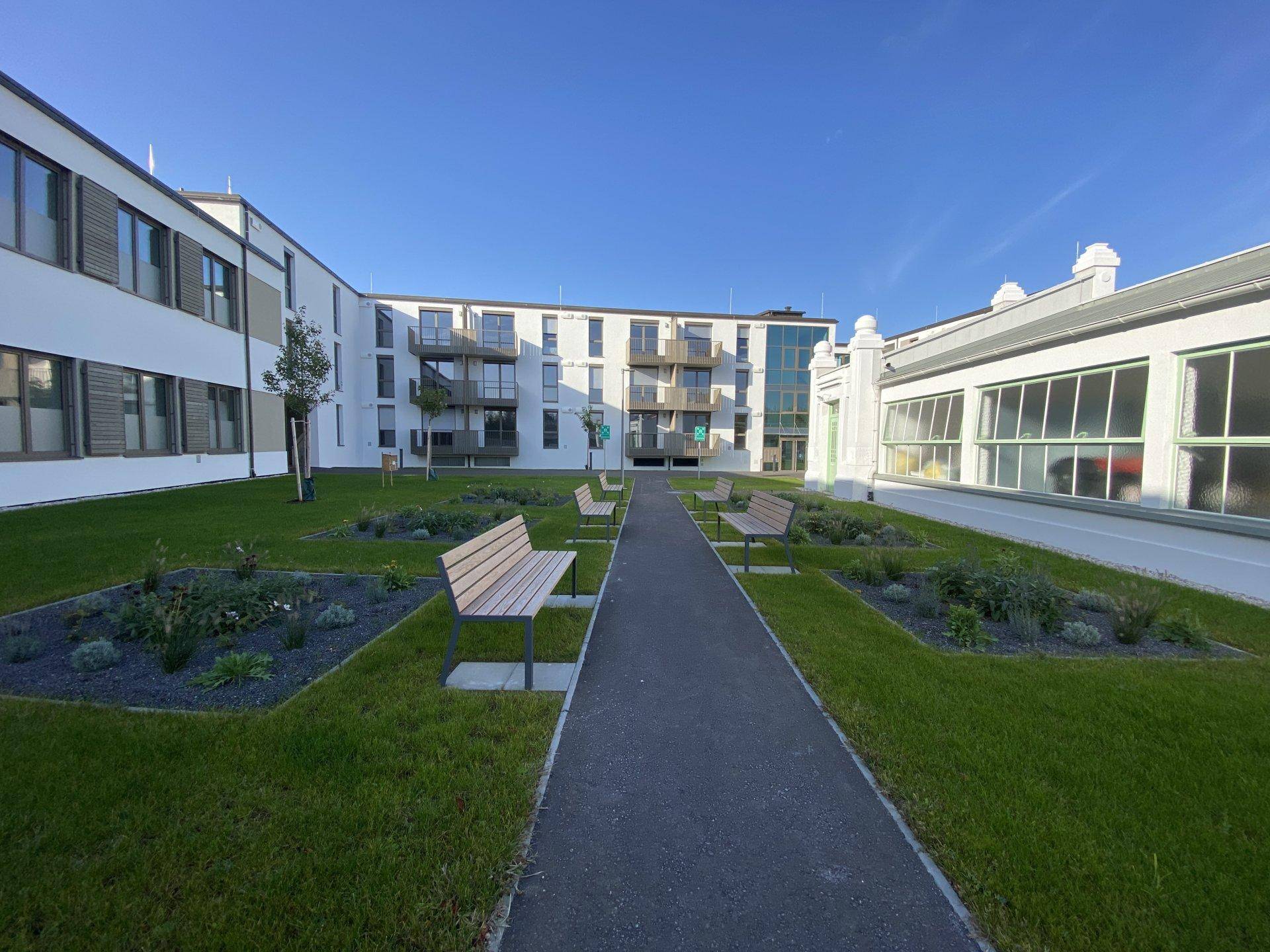 Gepflegter Innenhof mit Sitzbänken, Grünflächen und moderner Architektur der umliegenden Gebäude.