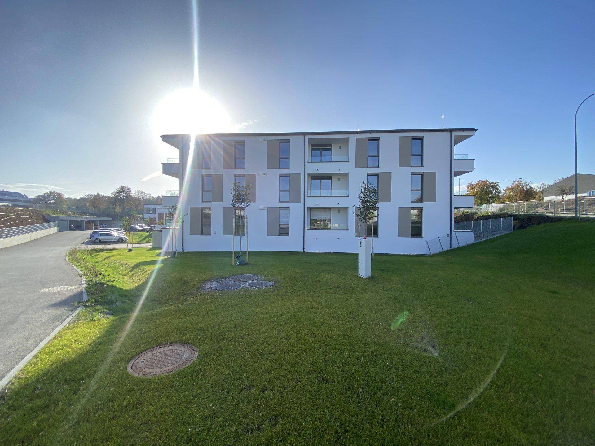 Modernes Wohngebäude mit weißer Fassade und Balkonen unter strahlendem Sonnenschein.