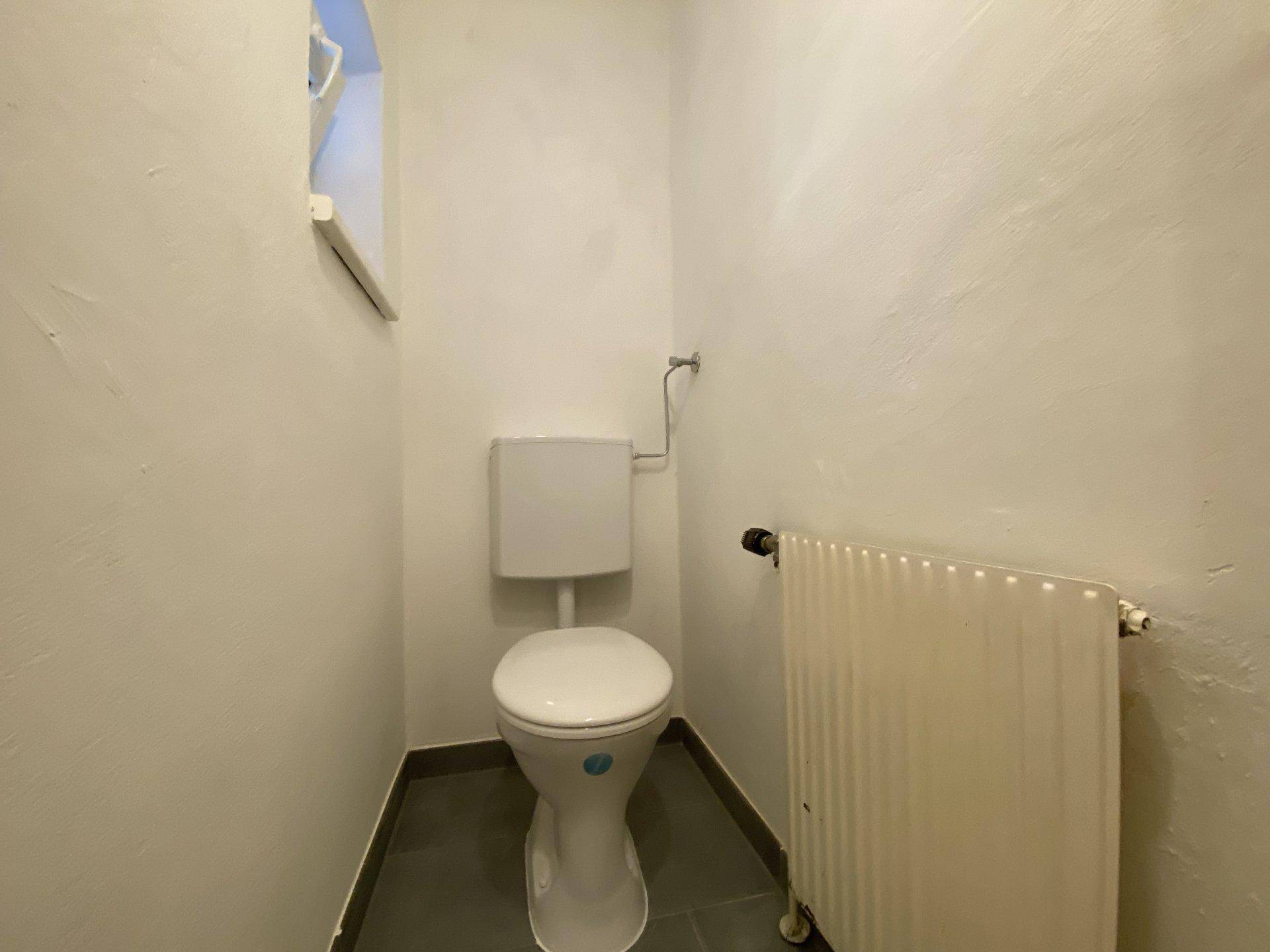 Separates WC mit Toilette, Heizkörper und kleinem Fenster.