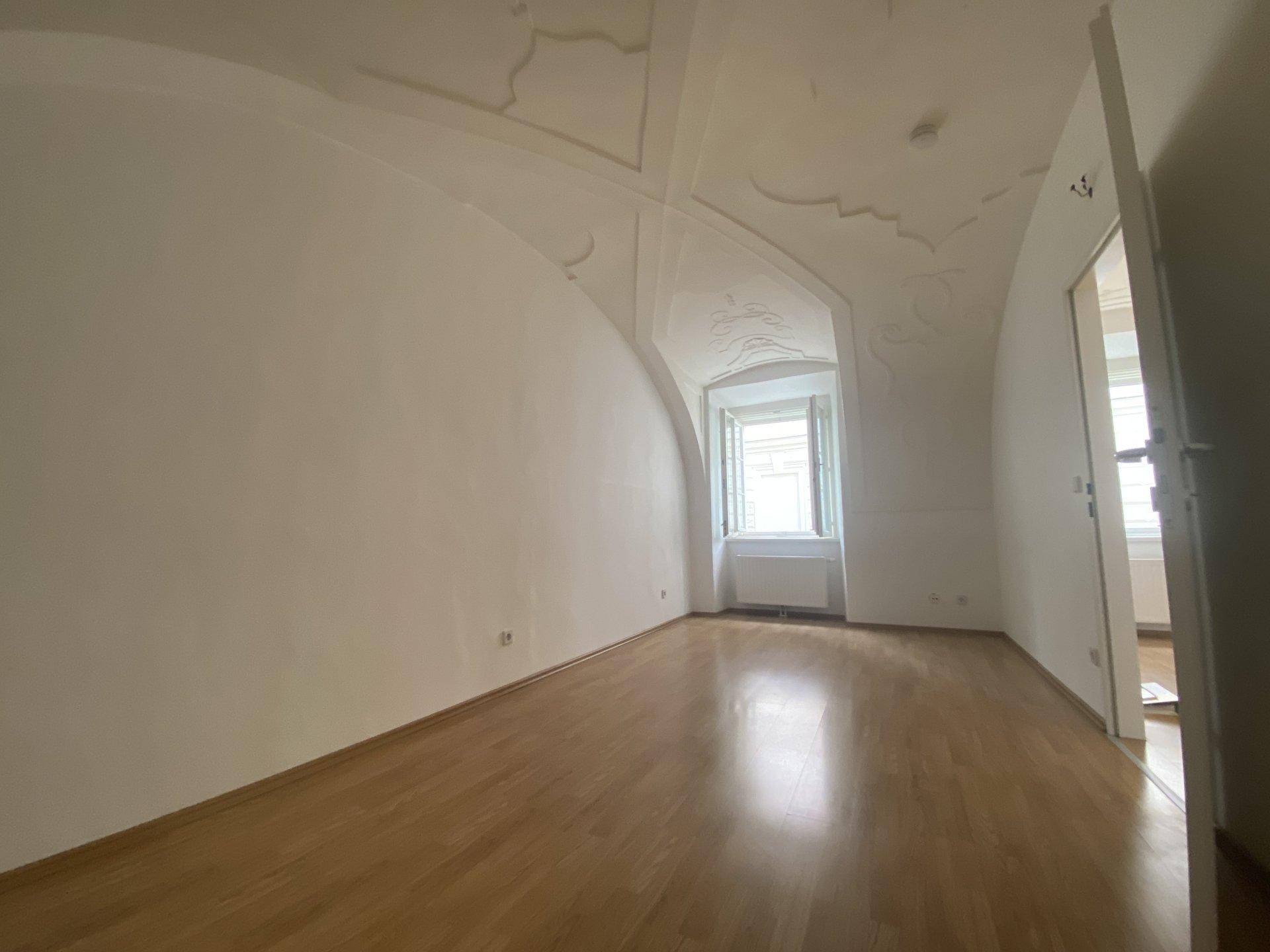 Helles Wohnzimmer mit eleganten Stuckverzierungen an der Decke und Holzboden.