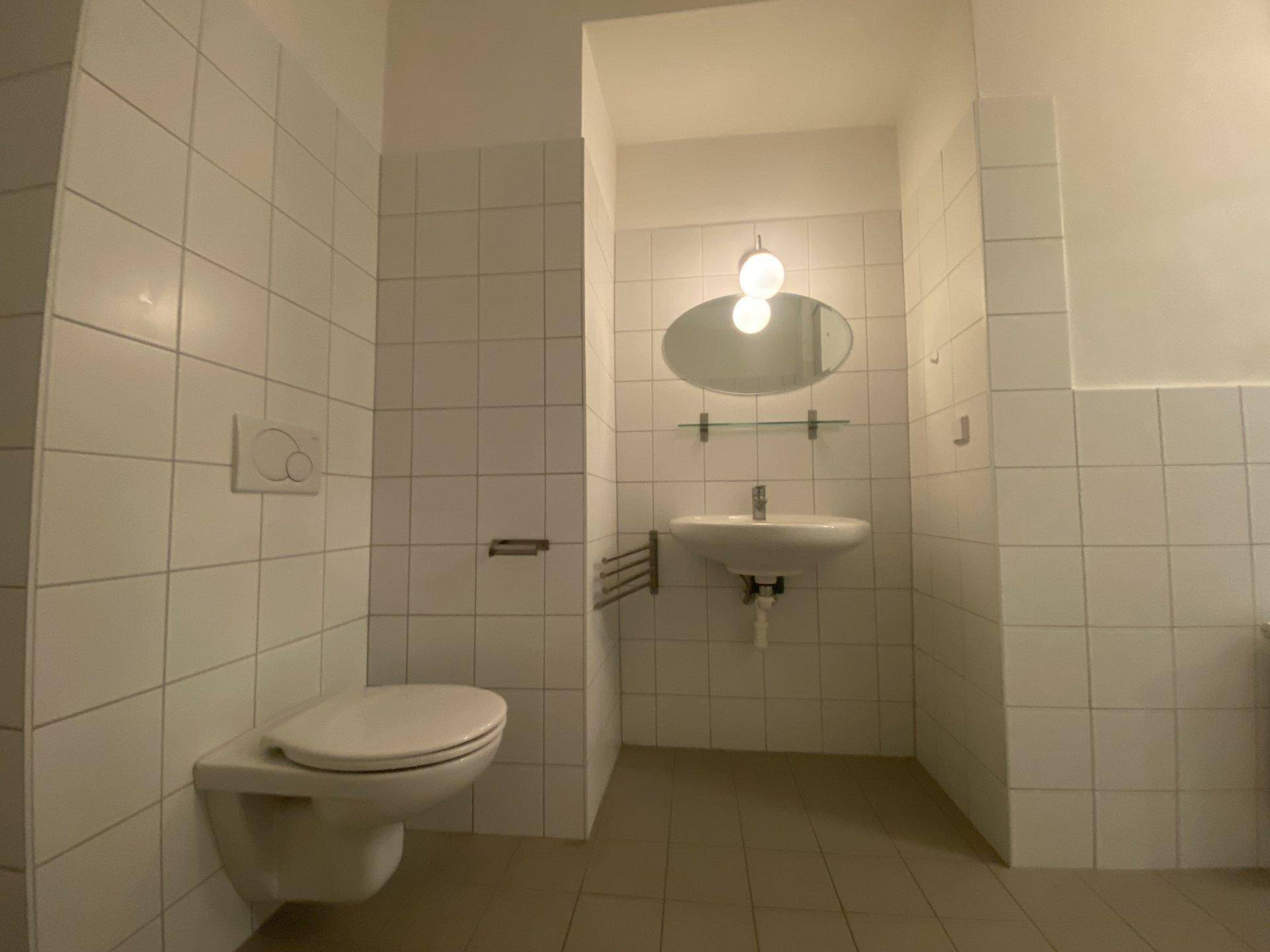 Funktionales Badezimmer mit wandhängendem WC, Waschbecken und Spiegel.