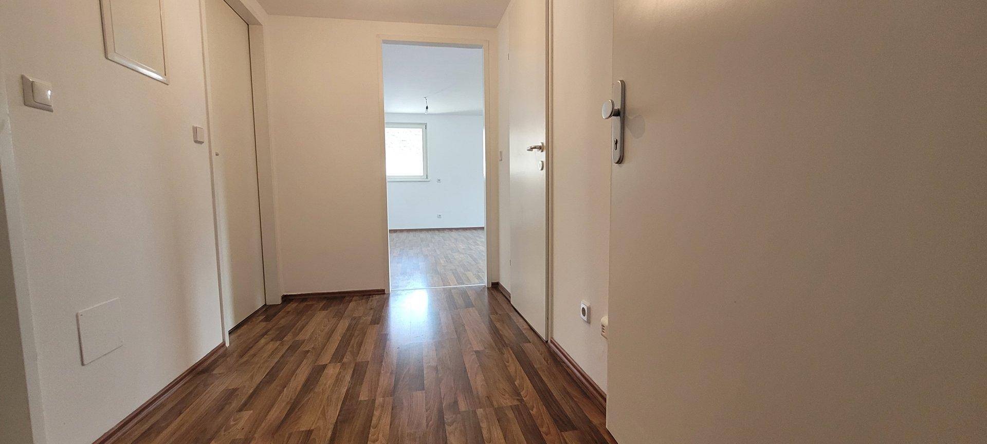 Heller Flur mit Holzboden und weißen Wänden, der zu weiteren Räumen führt.
