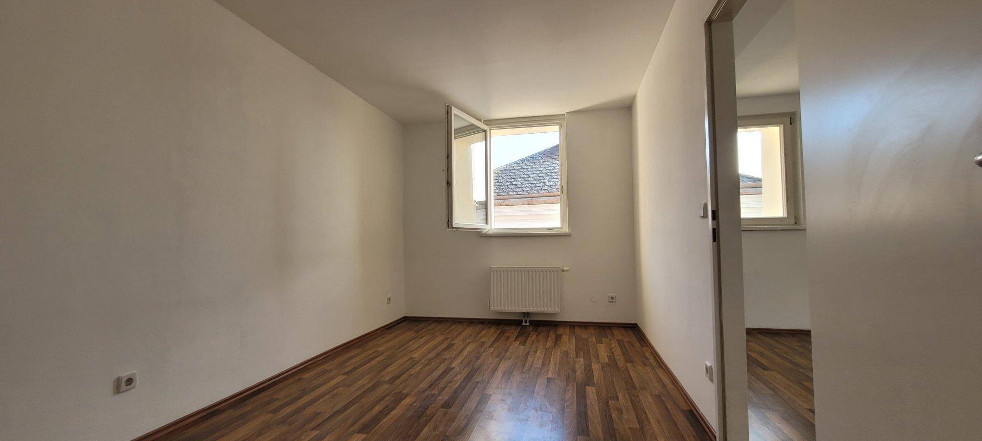 Helles Schlafzimmer mit Holzboden, weiß gestrichenen Wänden und einem Fenster.