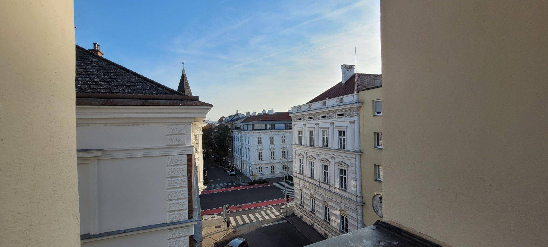 Blick aus dem Fenster auf eine belebte Stadtstraße mit historischen Gebäuden.