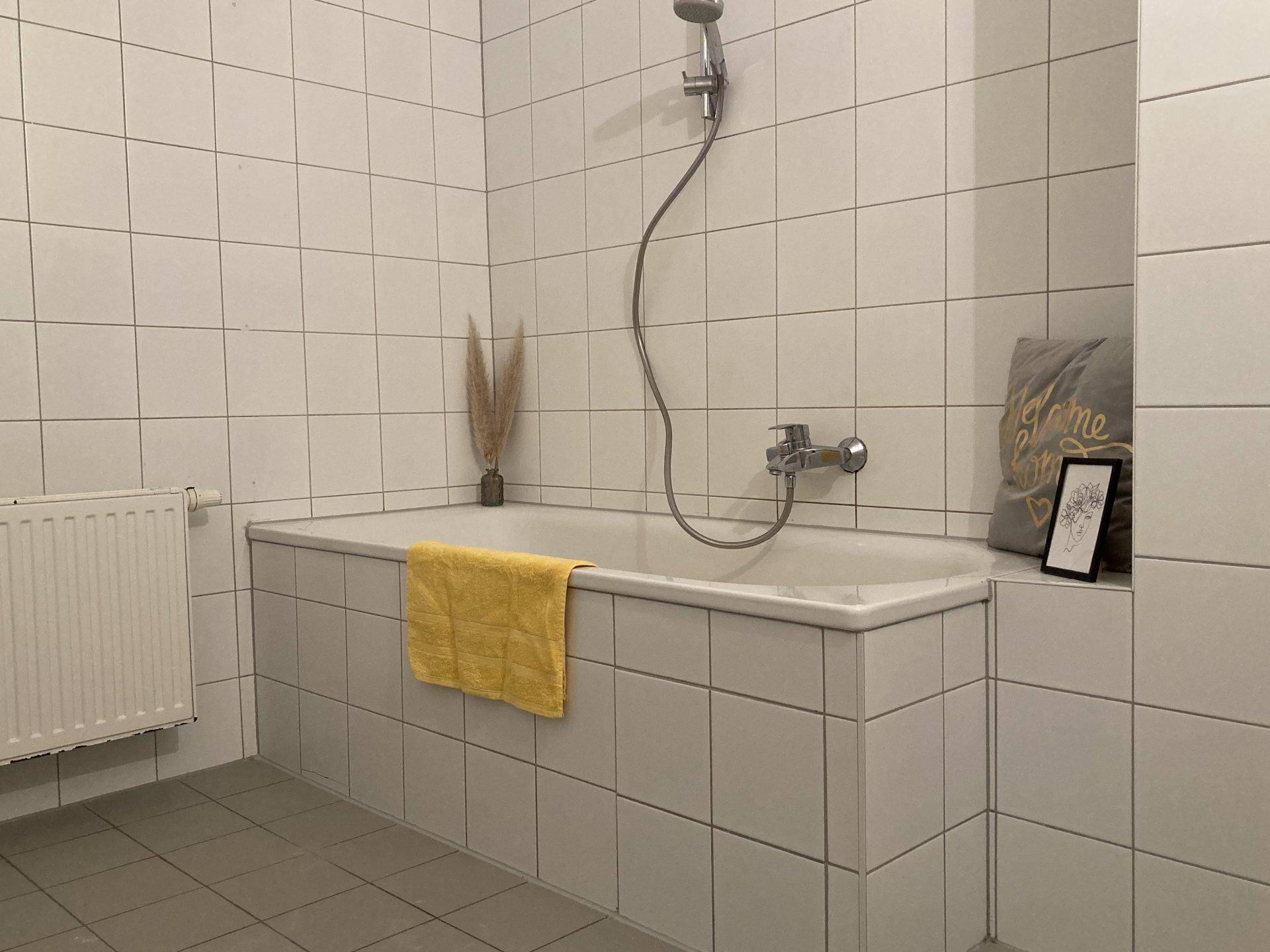 Modernes Badezimmer mit weiß gefliester Badewanne und Duscharmatur.