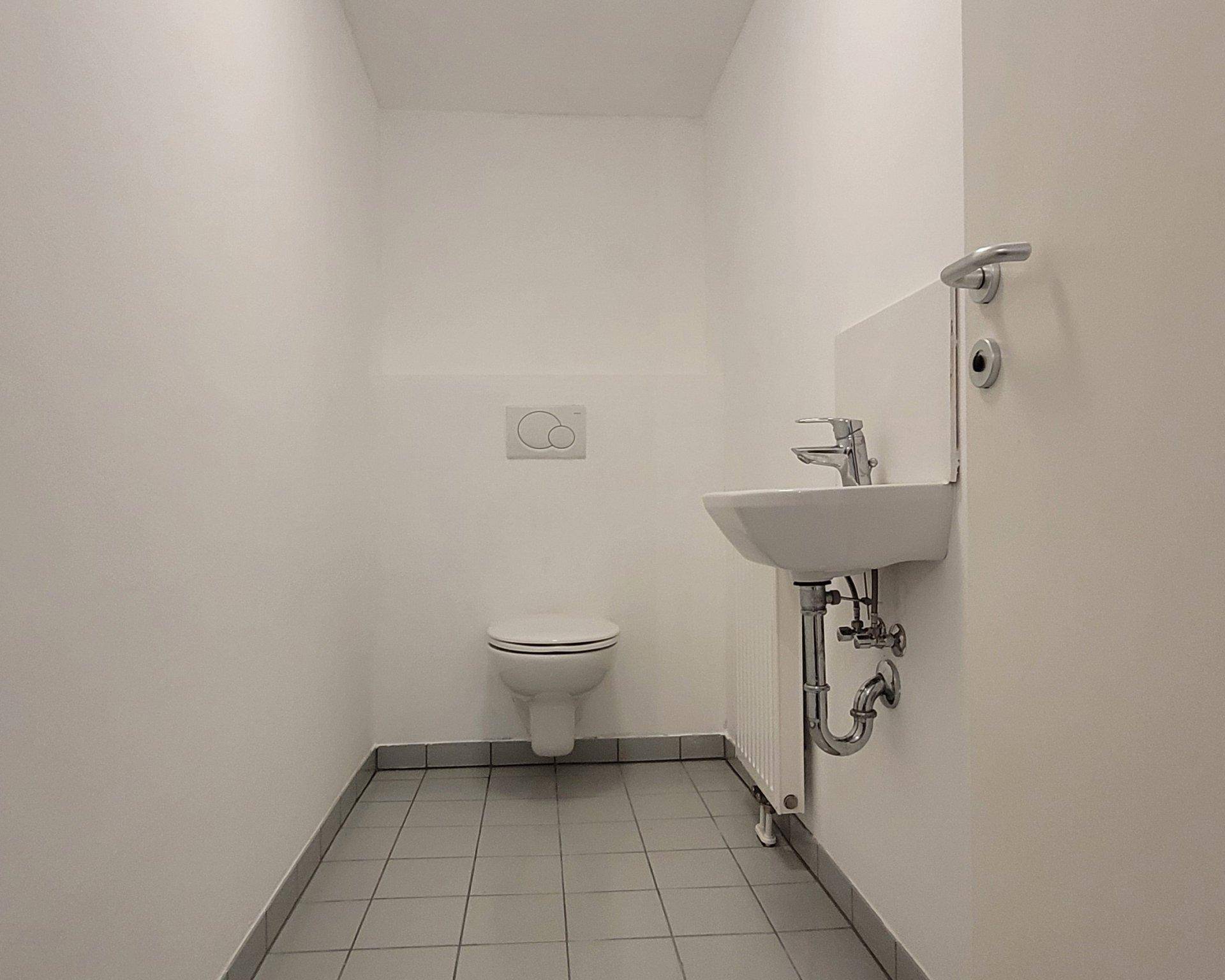 Separates WC mit wandhängender Toilette, kleinem Waschbecken und Heizkörper.