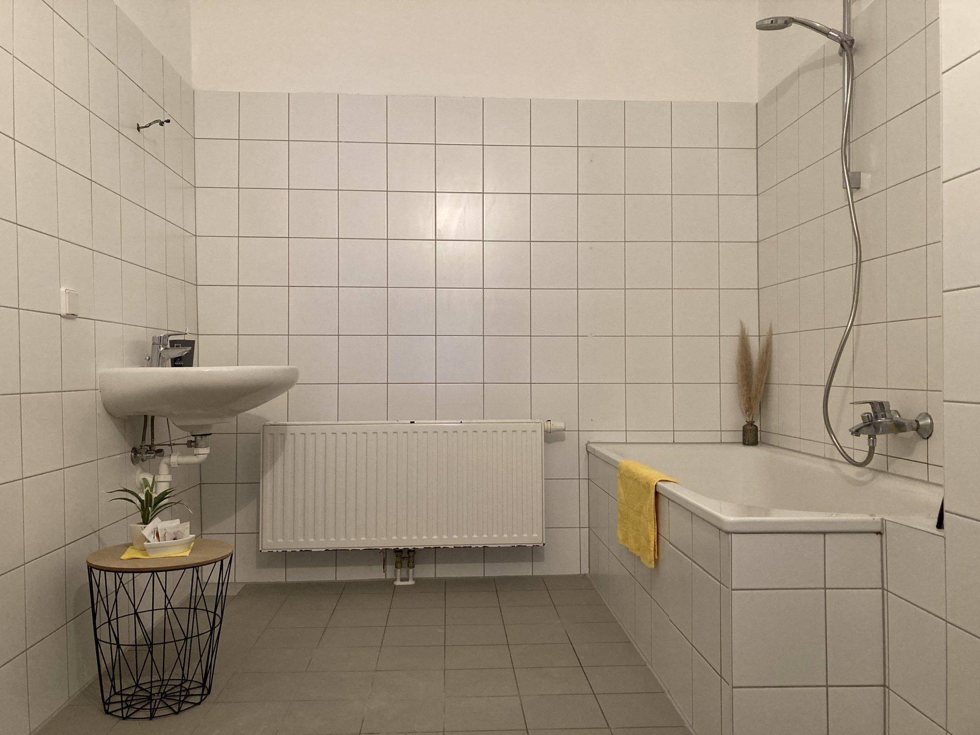 Gefliestes Badezimmer mit Badewanne, Waschbecken und Heizkörper in neutralen Farben.