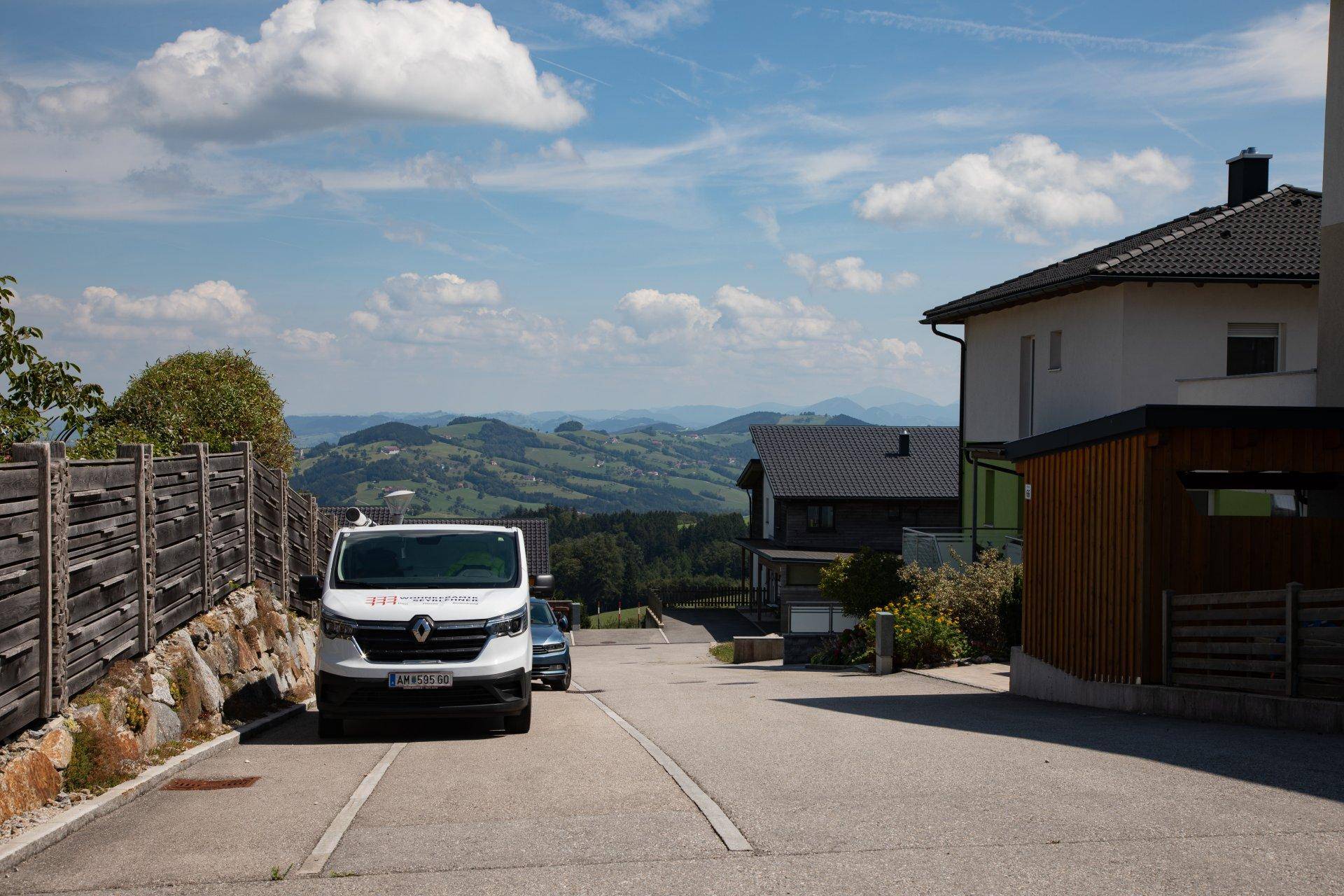 Wohnstraße mit geparktem Lieferwagen, Häusern und weitem Blick auf die bergige Landschaft.