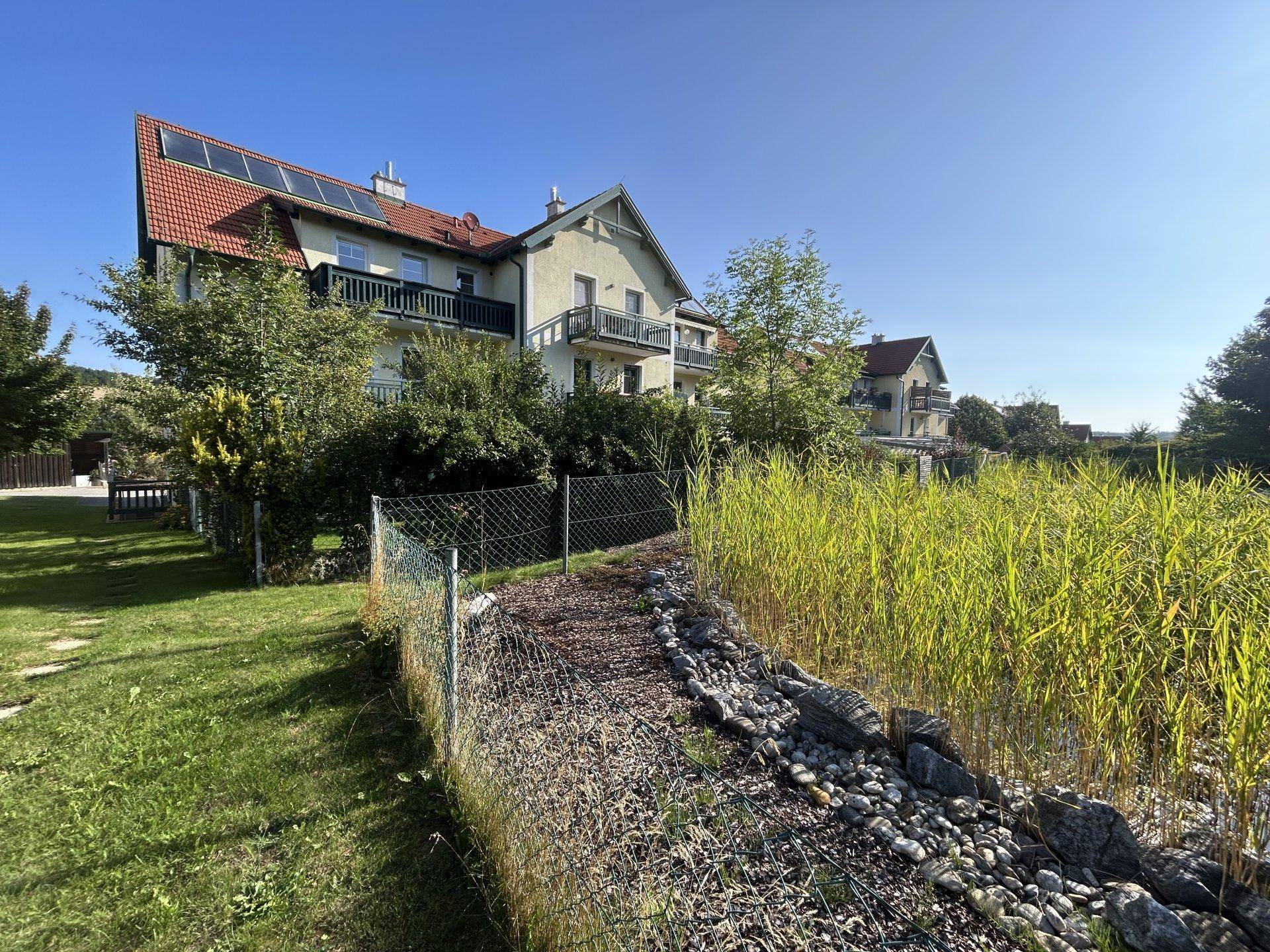 Hausfassade mit Balkonen und Solaranlage, umgeben von einem gepflegten Garten mit hohen Gräsern.