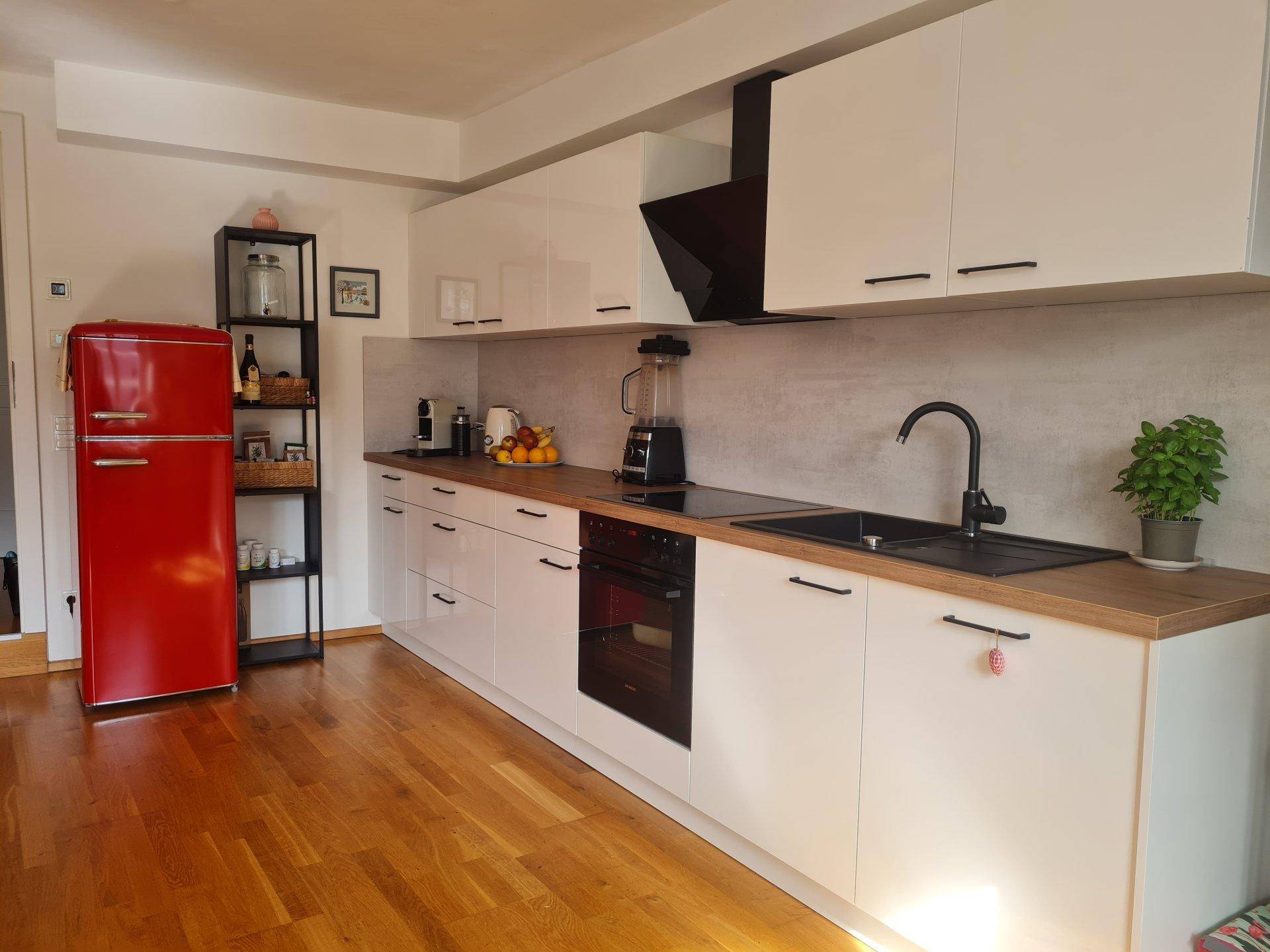 Moderne Küche mit weißen Hochglanzfronten, Holzarbeitsplatte und einem auffälligen roten Kühlschrank.