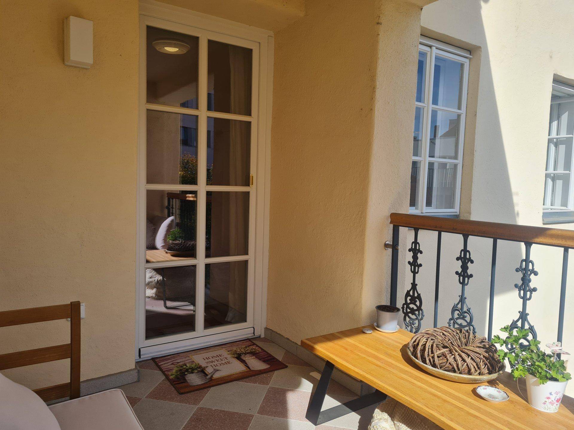 Sonniger Balkon mit Fliesenboden und einer Glastür, die den Zugang zum Innenraum ermöglicht.