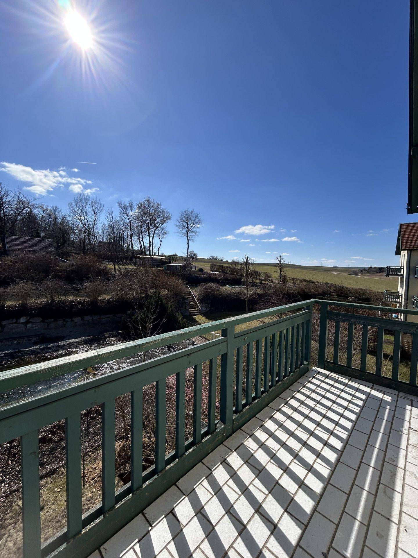 Sonniger Balkon mit Fliesenboden und weitem Blick über die ländliche Umgebung.