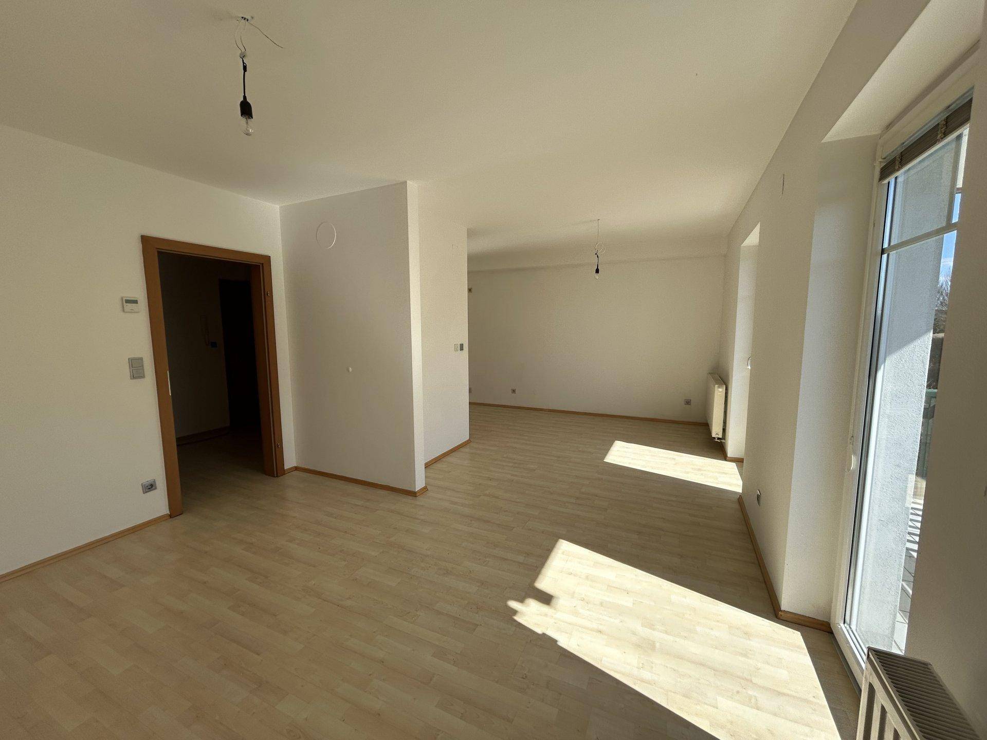 Lichtdurchflutetes Wohnzimmer mit Laminatboden und großem Fenster, bereit zur Einrichtung.