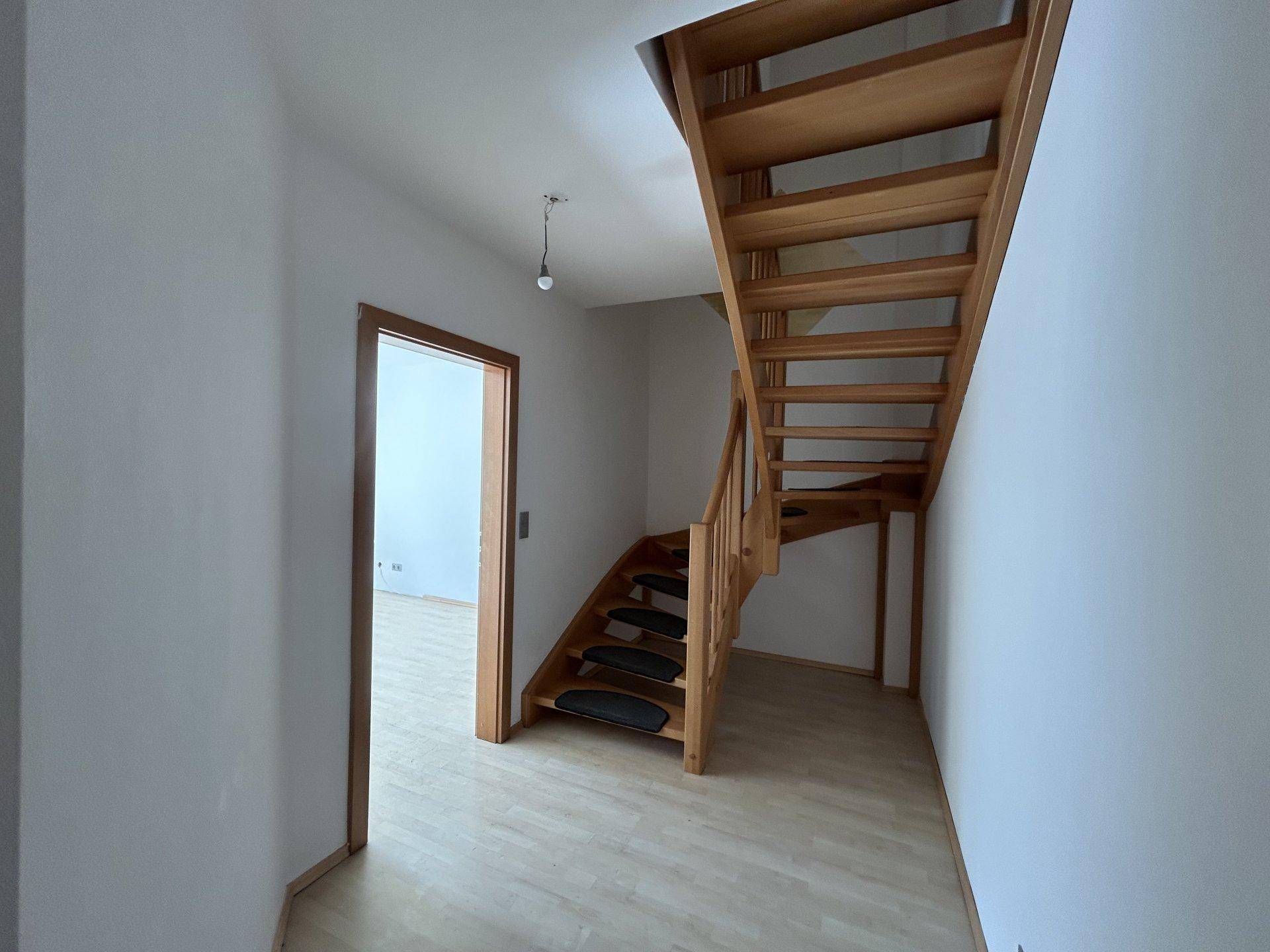 Heller Flur mit Holztreppe und Laminatboden, der die verschiedenen Ebenen verbindet.