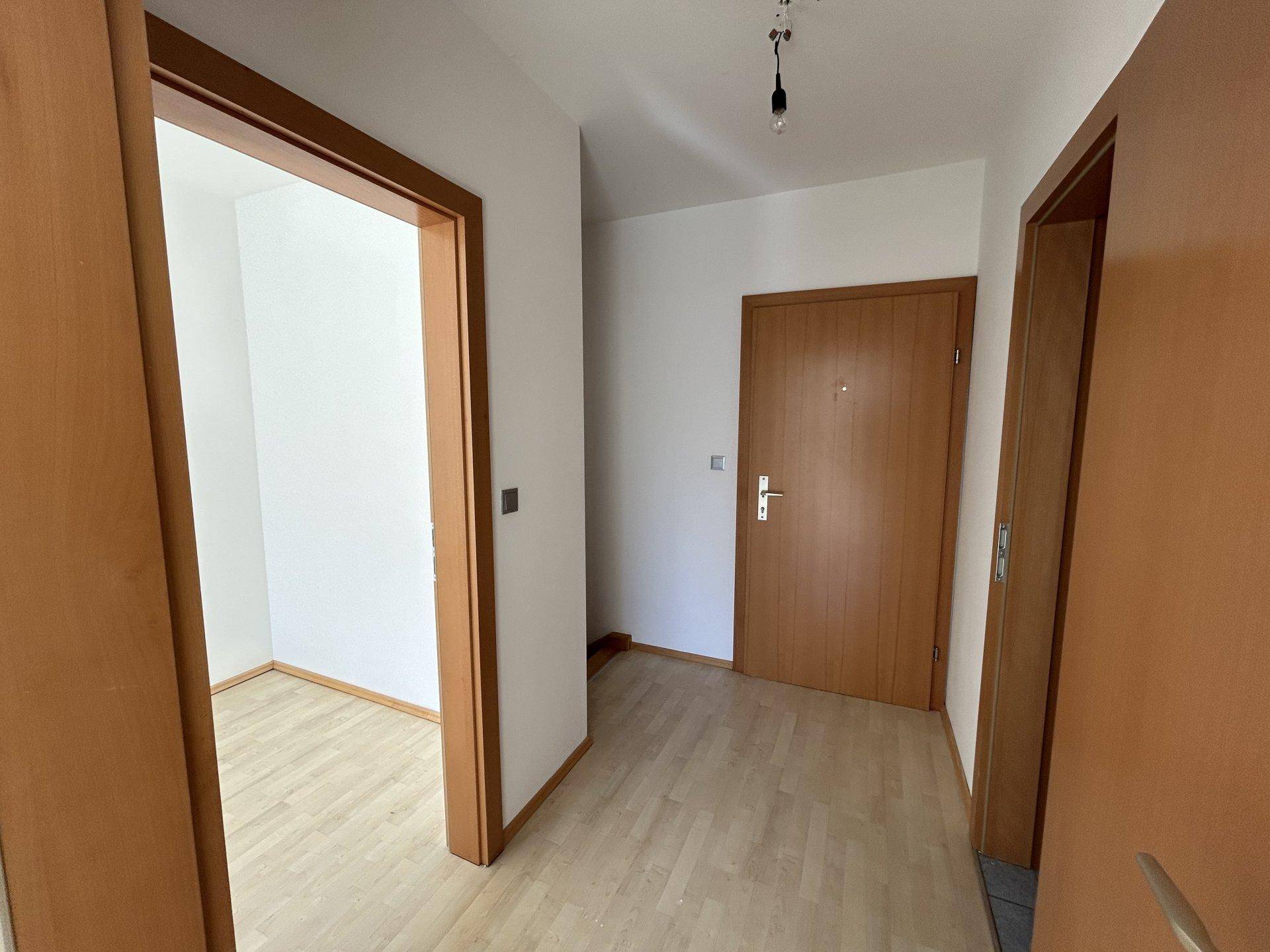 Eingangsbereich mit Holztüren und Laminatboden, der zu den angrenzenden Räumen führt.