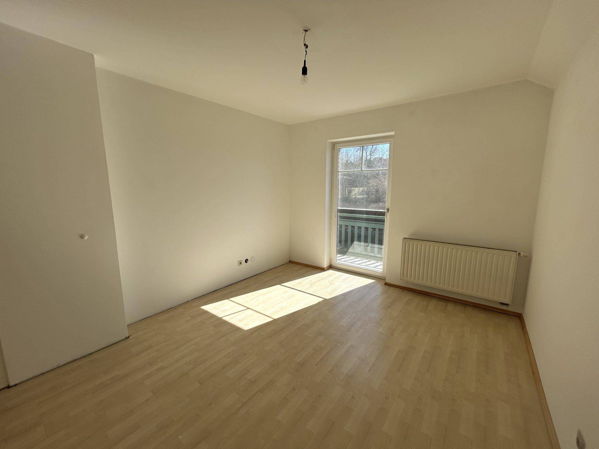Helles Schlafzimmer mit Laminatboden, Heizkörper und Zugang zu einem französischen Balkon.