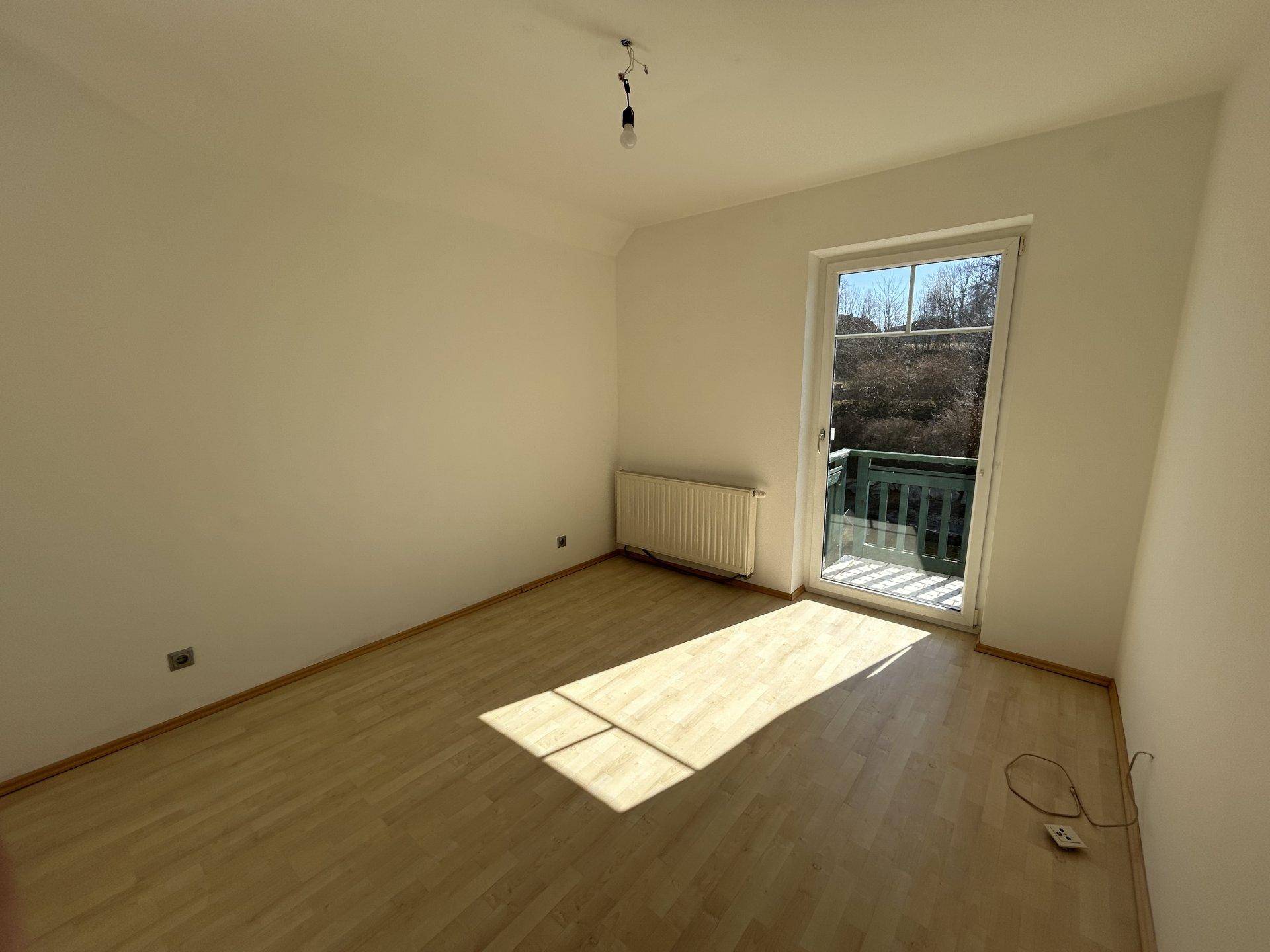 Sonniger Raum mit Laminatboden und Fenster, das viel Tageslicht hereinlässt.