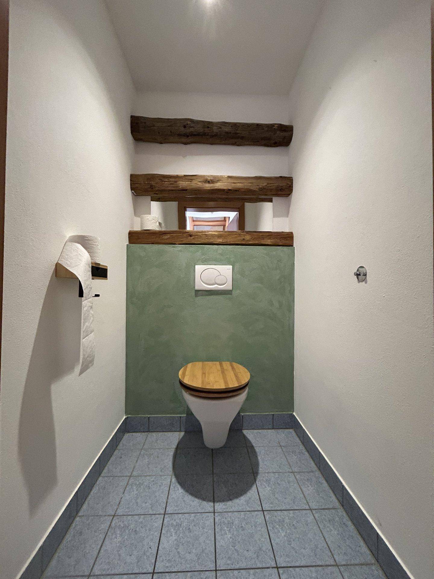 Separate Toilette mit grüner Akzentwand, Holzdetails und Fliesenboden.