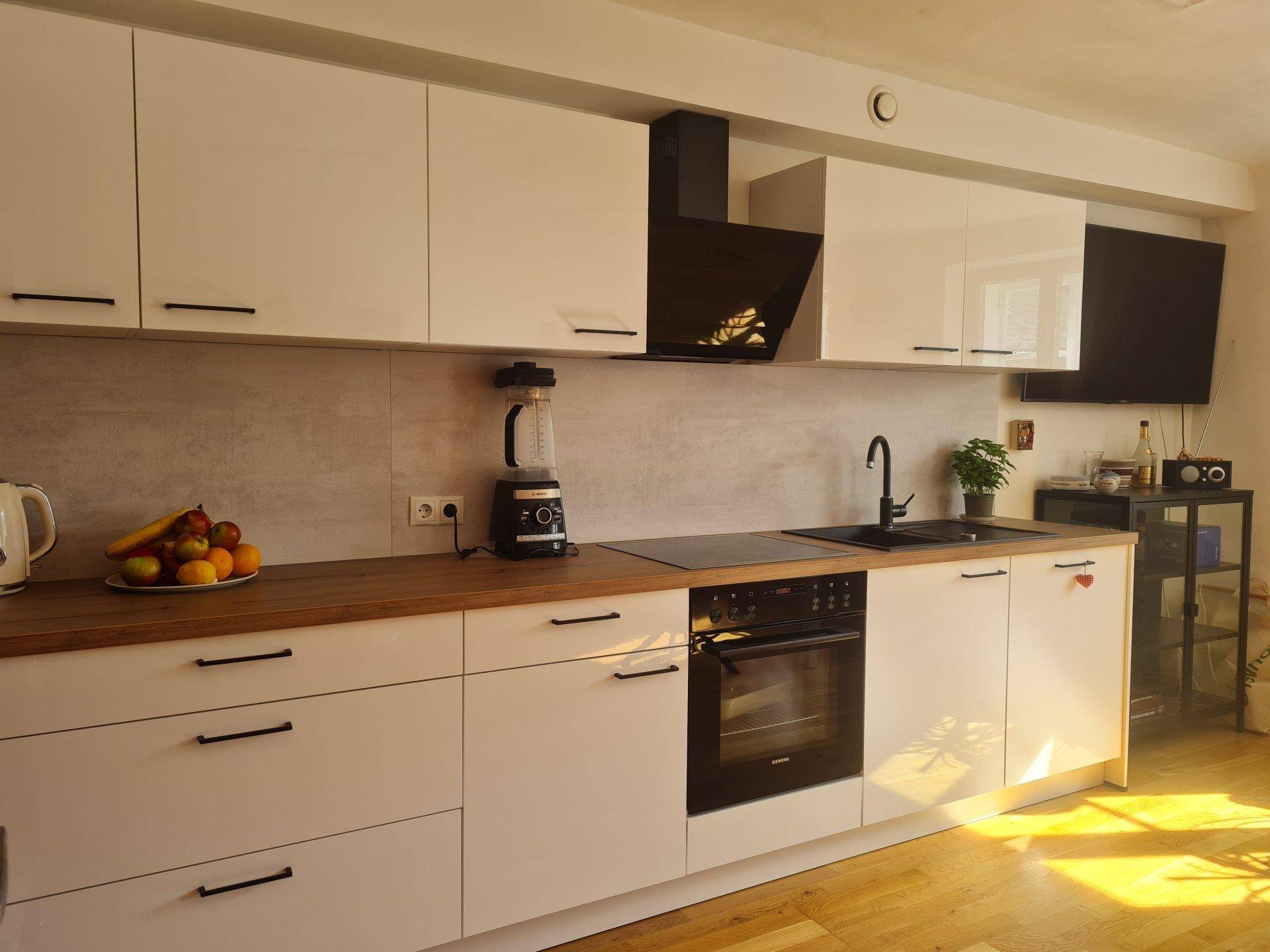 Detailansicht der modernen Küche mit Induktionskochfeld, Backofen und schwarzer Spüle.