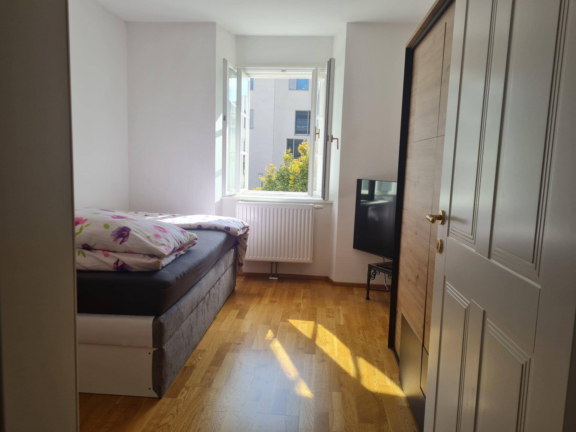 Gemütliches Schlafzimmer mit Holzboden und einem Fenster, das den Raum mit Licht füllt.