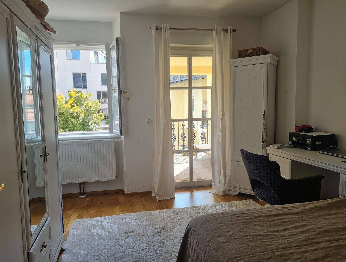 Schlafzimmer mit Holzboden, weißen Kleiderschränken und Zugang zu einem französischen Balkon.