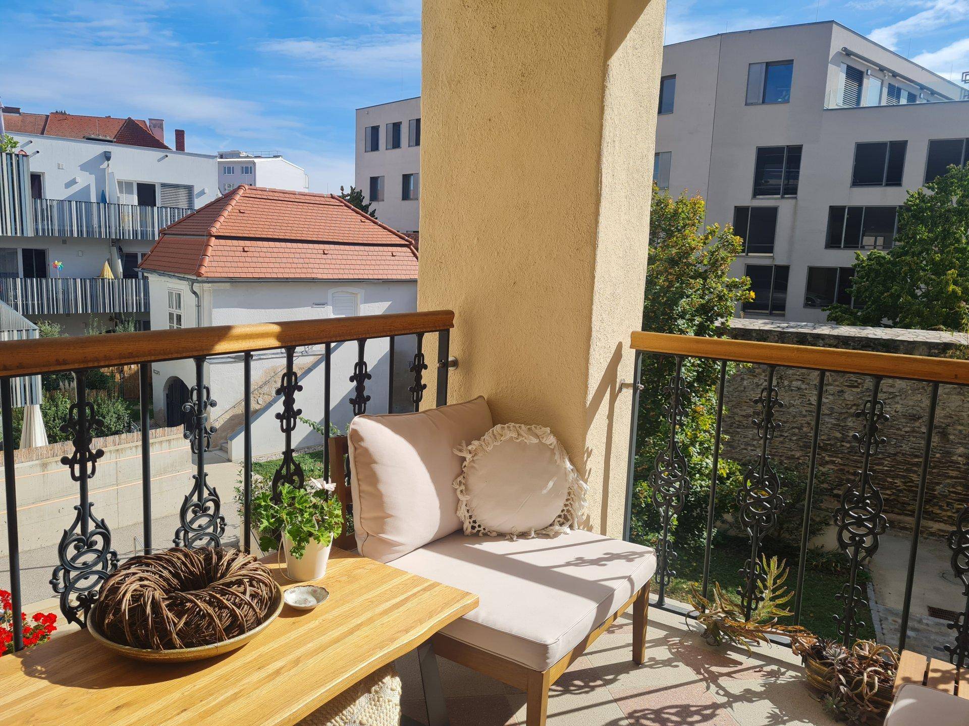 Sonniger Balkon mit schmiedeeisernem Geländer und Ausblick auf die städtische Umgebung.