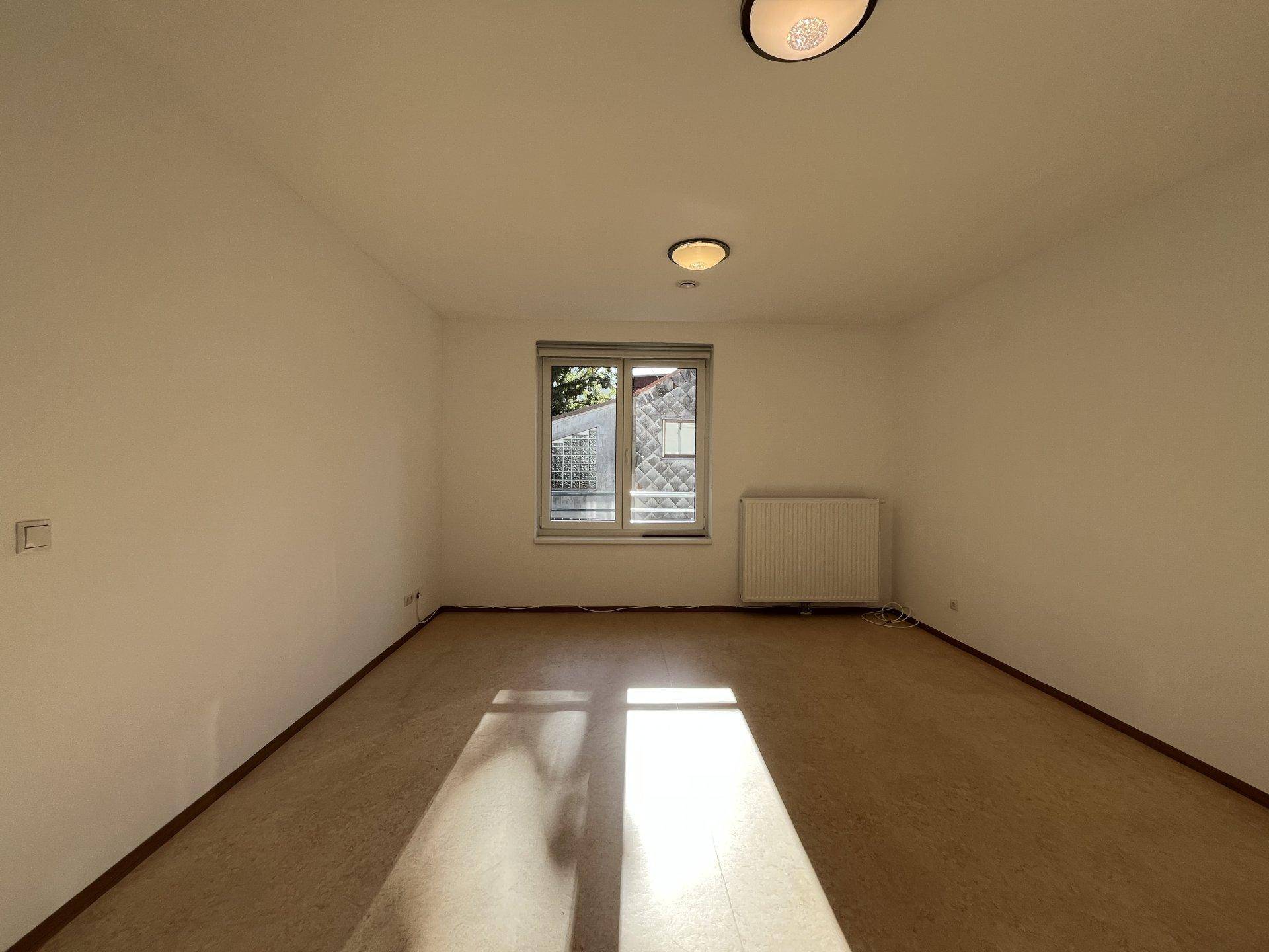 Leerer Raum mit hellem Boden, einem Fenster und Heizkörper, bereit zur individuellen Gestaltung.